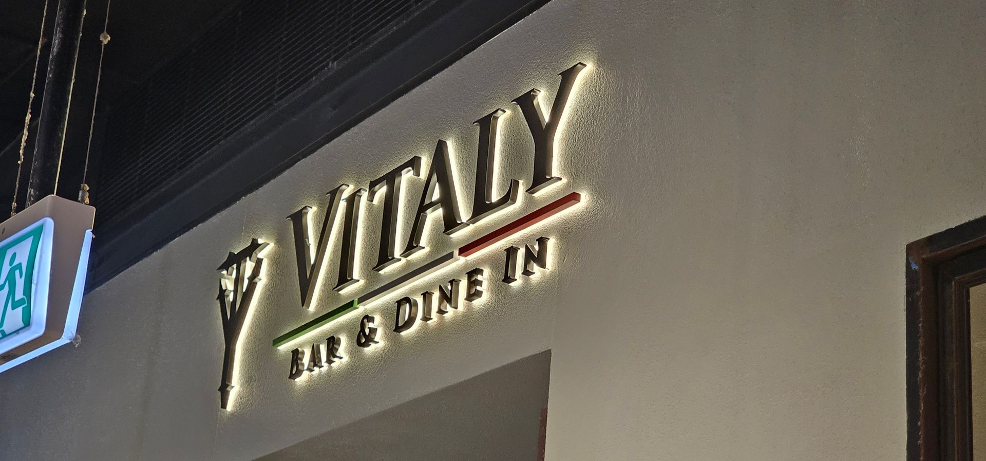 Lit sign for “VITALY” and “BAR & DINNER” on a building facade at night