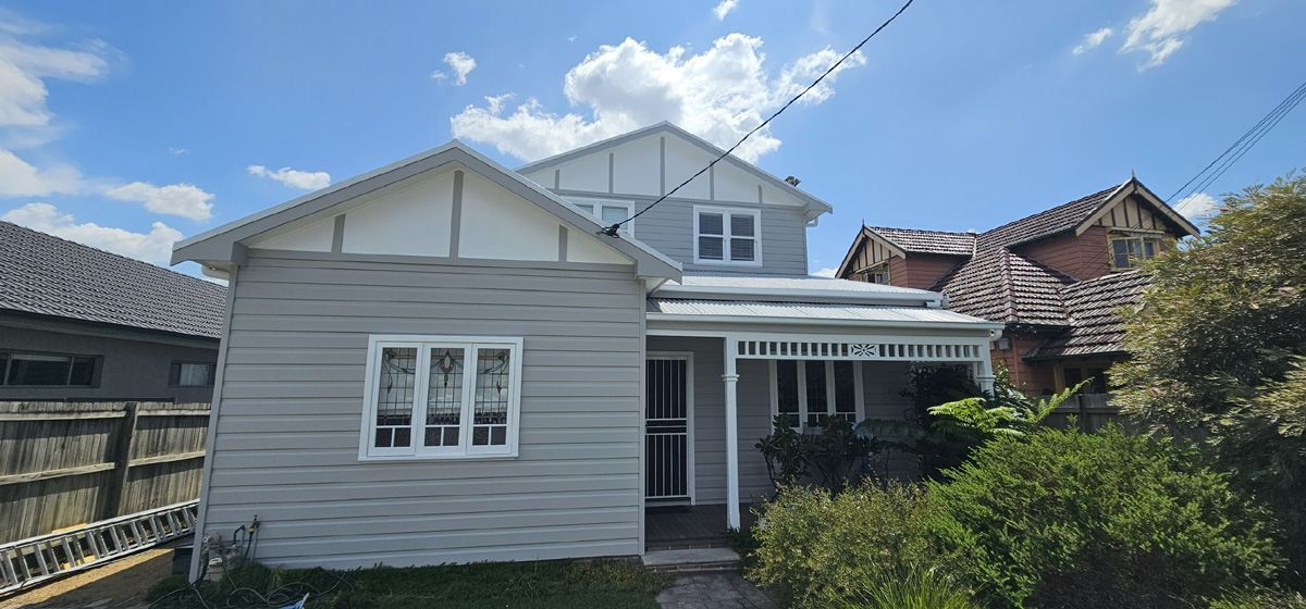 Small gray house with white trim and a front porch under a blue sky