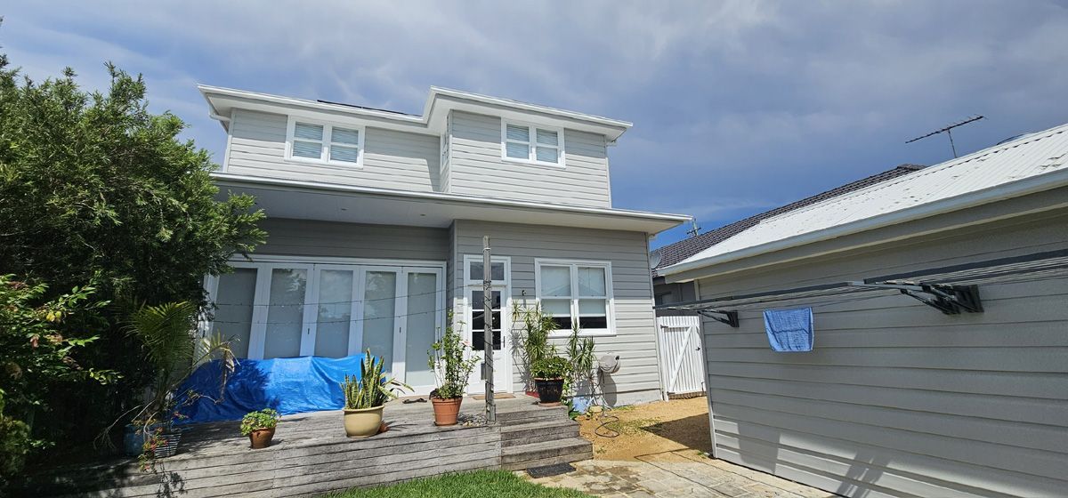 Two-story white house with blue awnings and a gray garage under a bright blue sky
