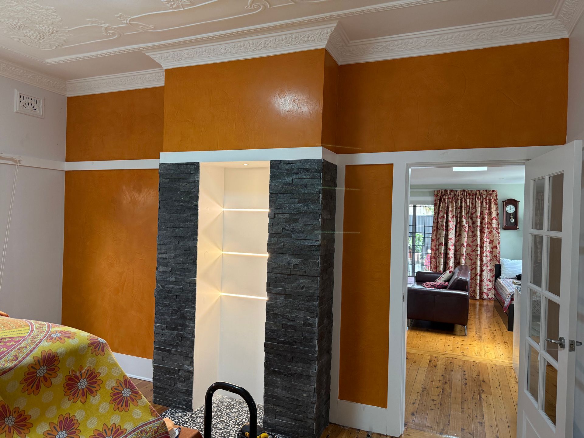 Orange-walled room with a white fireplace, stone accents, and an open doorway to a hallway and living area