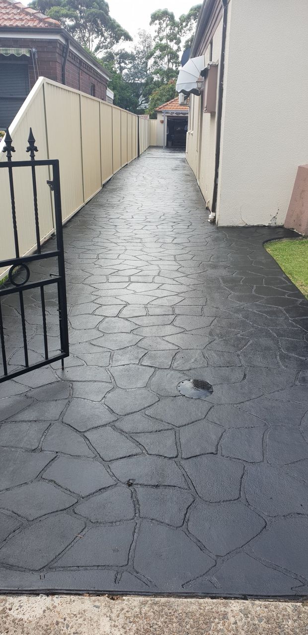 Narrow wet stone walkway between houses and a fence, leading into the distance.