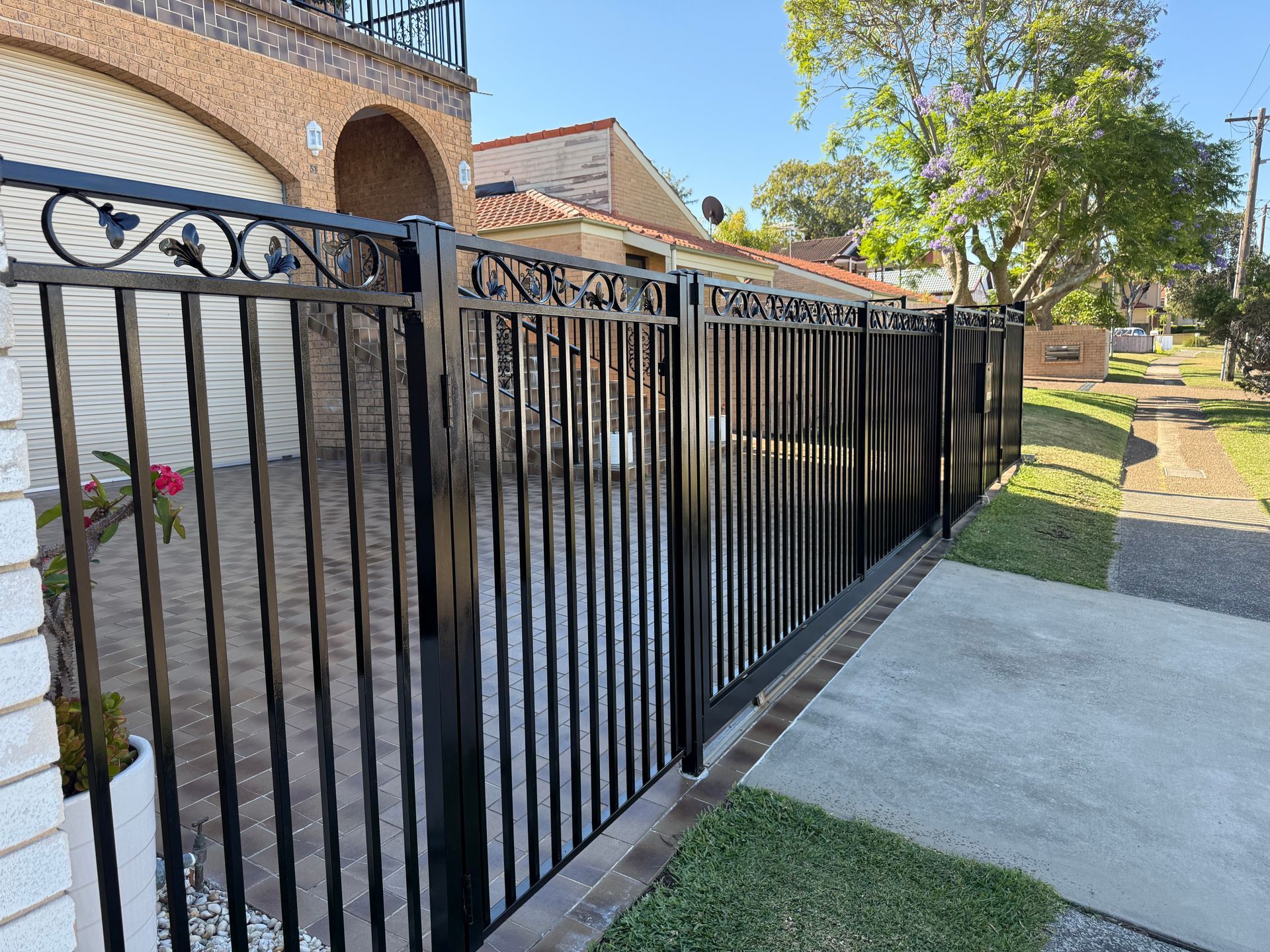 Black metal fence beside a sidewalk and brick apartment building in a sunny residential area