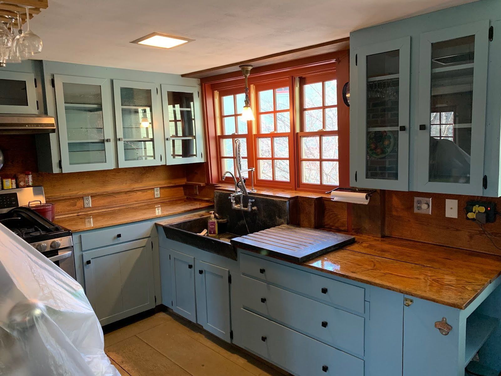 Modern kitchen with light blue cabinets, wood countertops, and a large window over the sink.