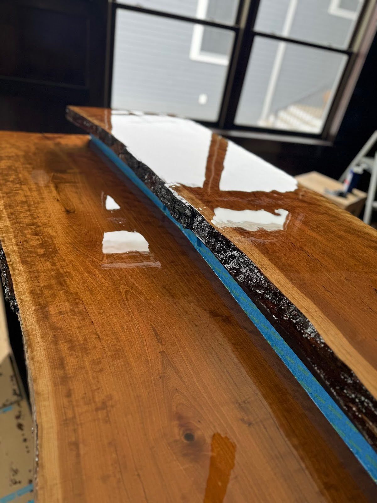 Glossy wooden tabletop with blue painter’s tape along the edge near a window