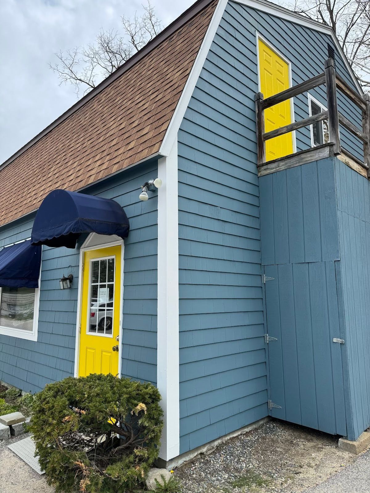 Blue storefront with yellow door and window, navy awning, and sloped shingle roof.