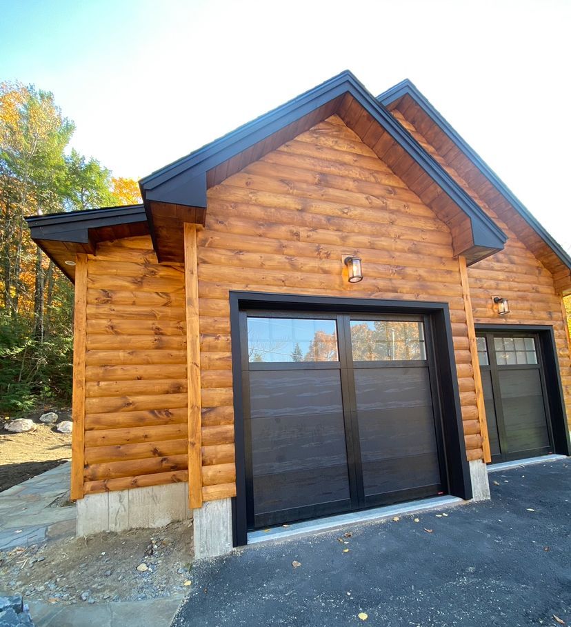 A log cabin with two garage doors and a black roof.