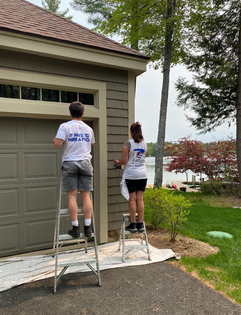 A man on a ladder paints the side of a house