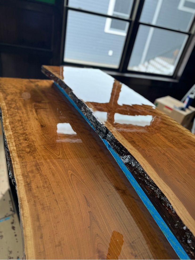 Polished wooden tabletop with blue tape along the edge and a reflective finish near a window