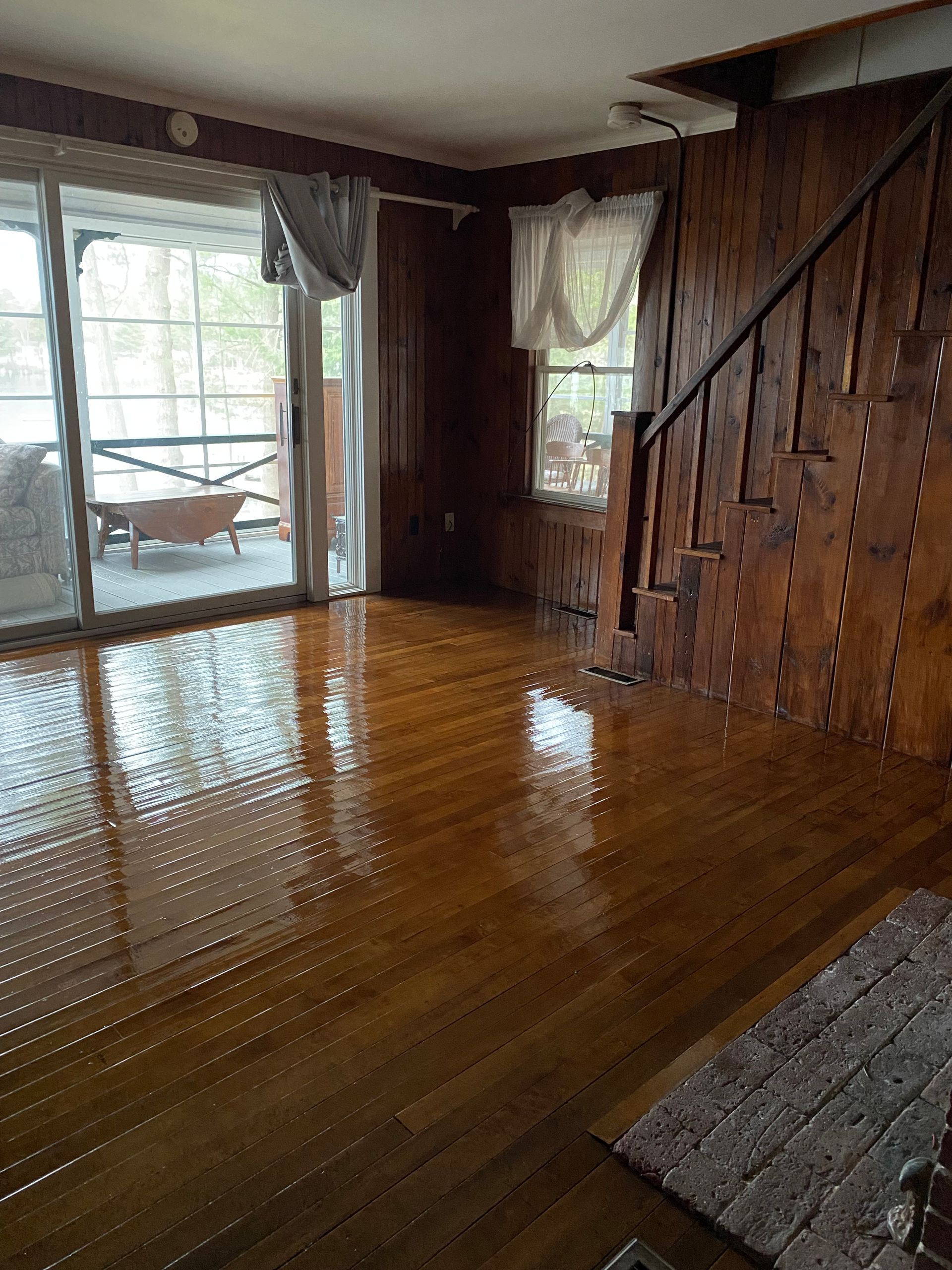 Empty wood-paneled room with shiny hardwood floor and sliding glass door to a patio.