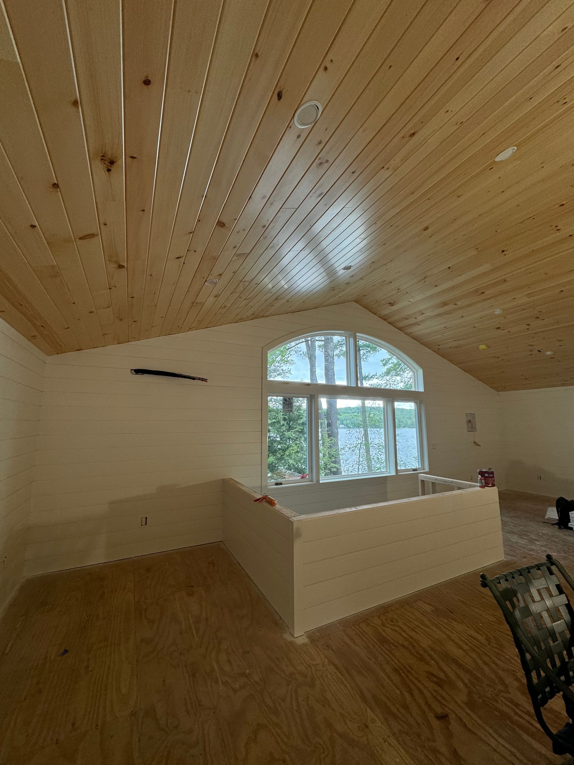 Empty room with slanted wooden ceiling, arched window, and light wood flooring.