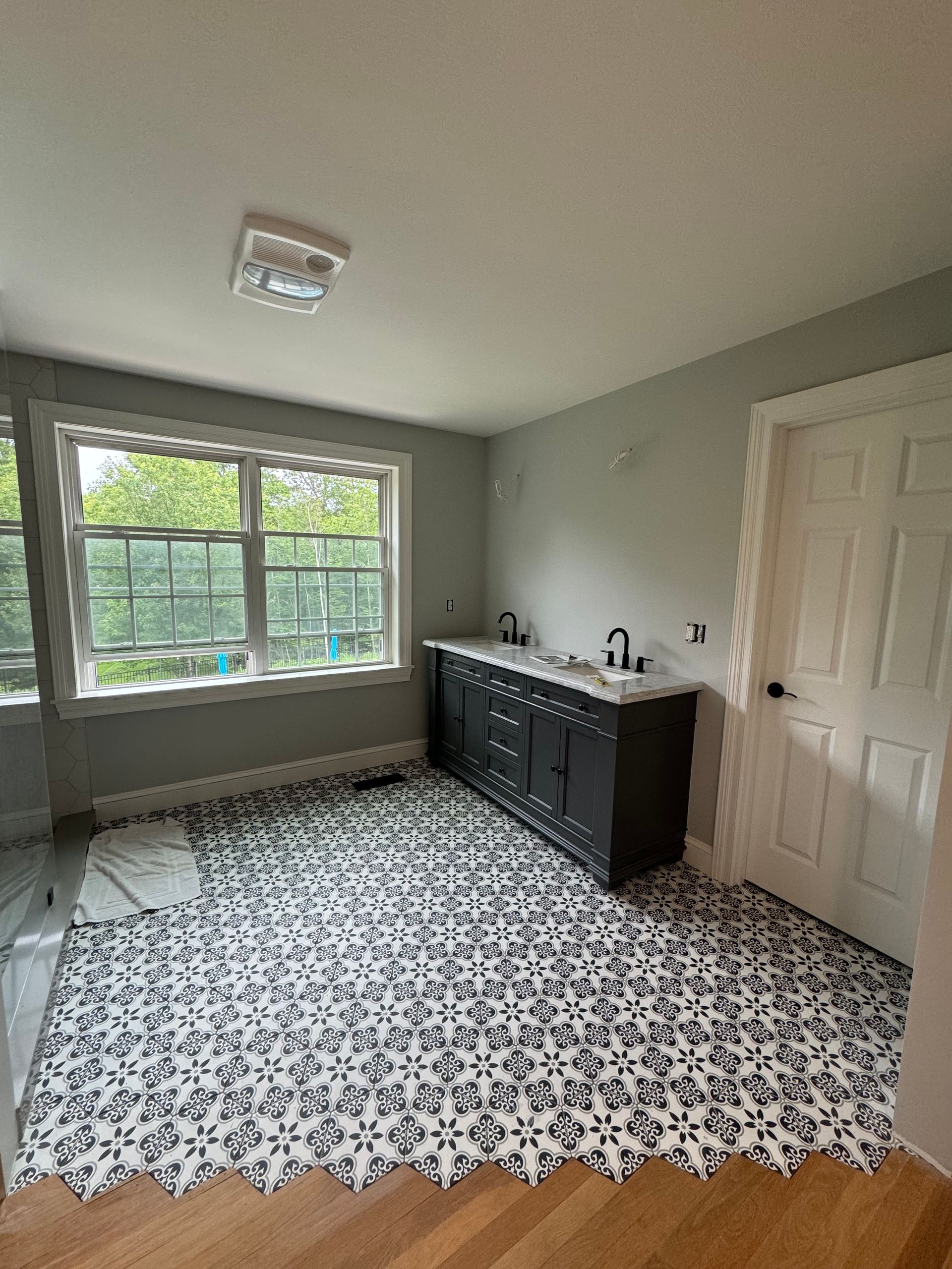 Empty room with patterned tile floor, black sideboard, white door, and a window overlooking greenery