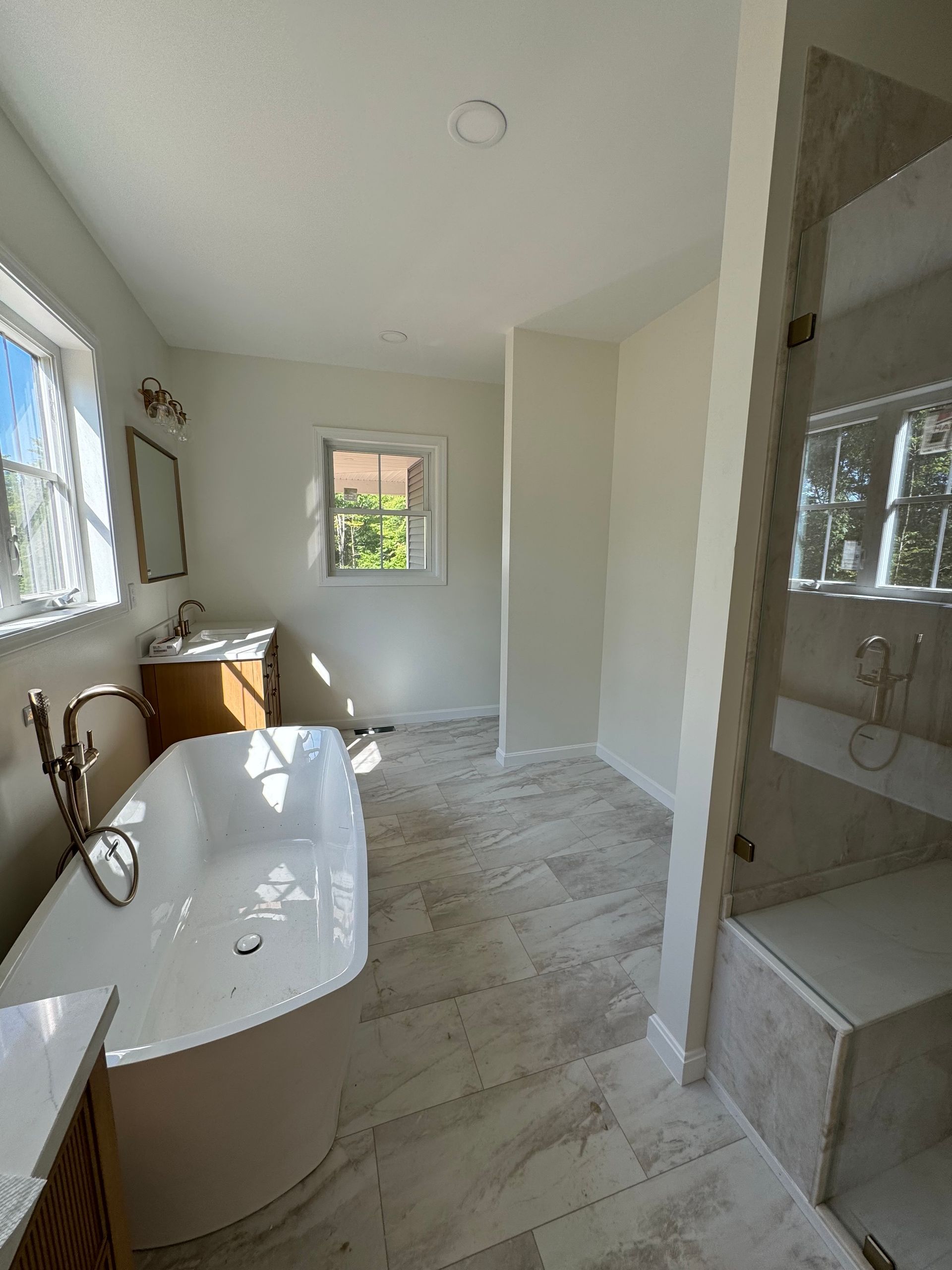 Bright bathroom with a soaking tub, shower, sink, and two windows with white curtains.