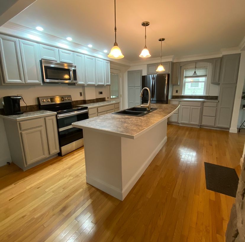 Modern kitchen with white cabinets, stainless appliances, island, pendant lights, and hardwood floors