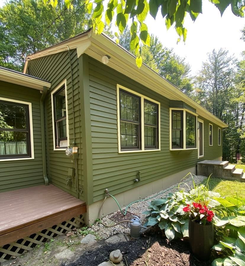 Green house exterior with windows, a small porch, and flowers in a sunny yard