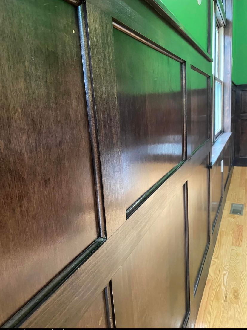 Dark wood-paneled wall in a hallway with a hardwood floor and a window at the end