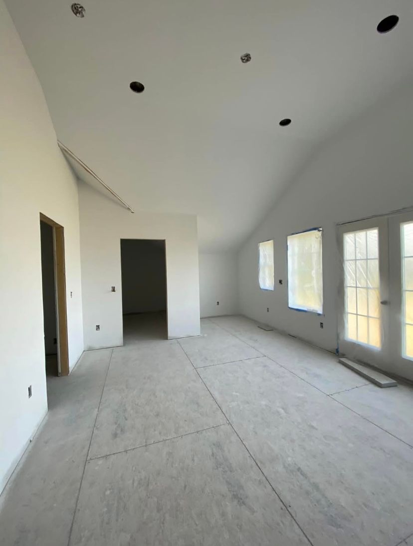 Empty unfinished room with white walls, bare floors, recessed ceiling lights, and multiple windows and doors