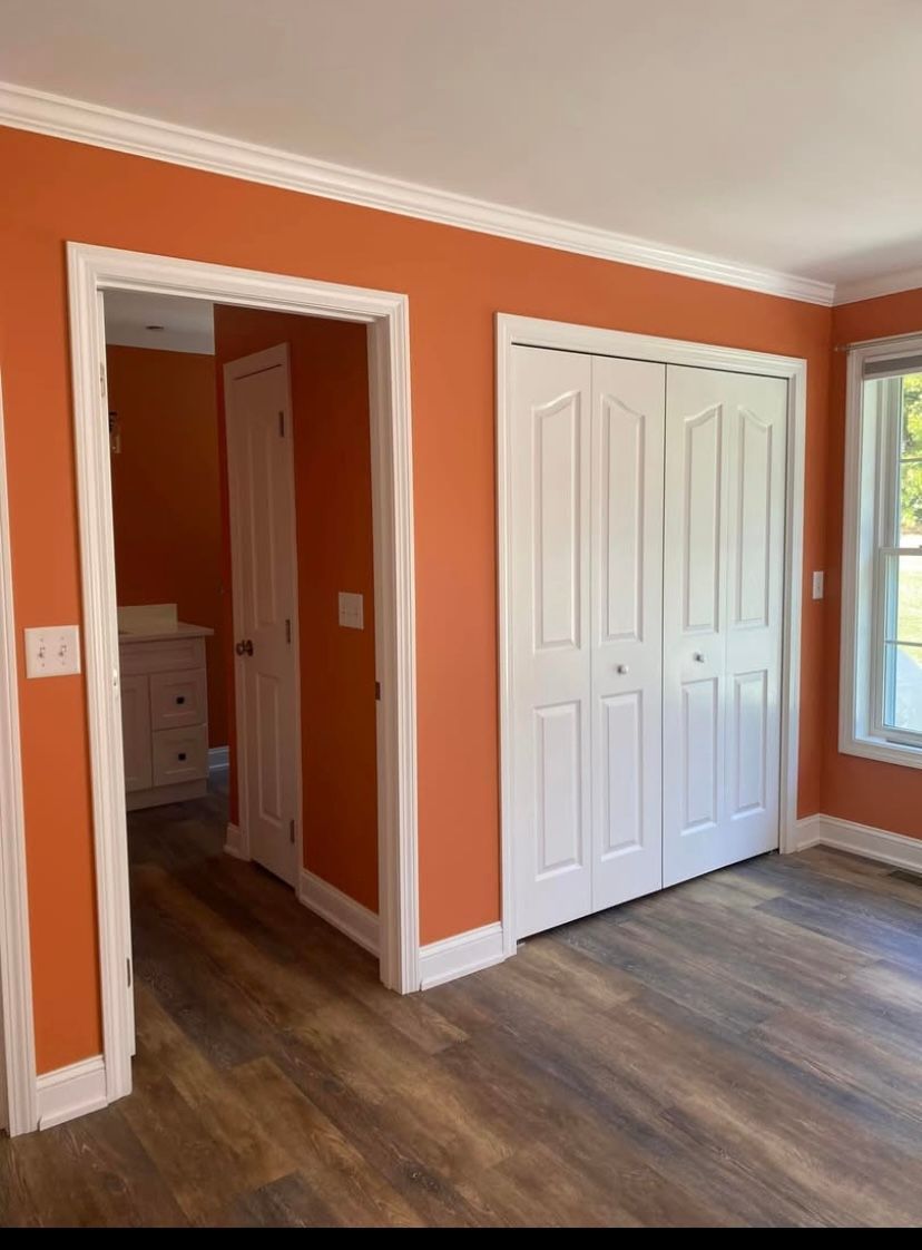 Orange bedroom with white closet doors, doorway to hall, and wood-look flooring.