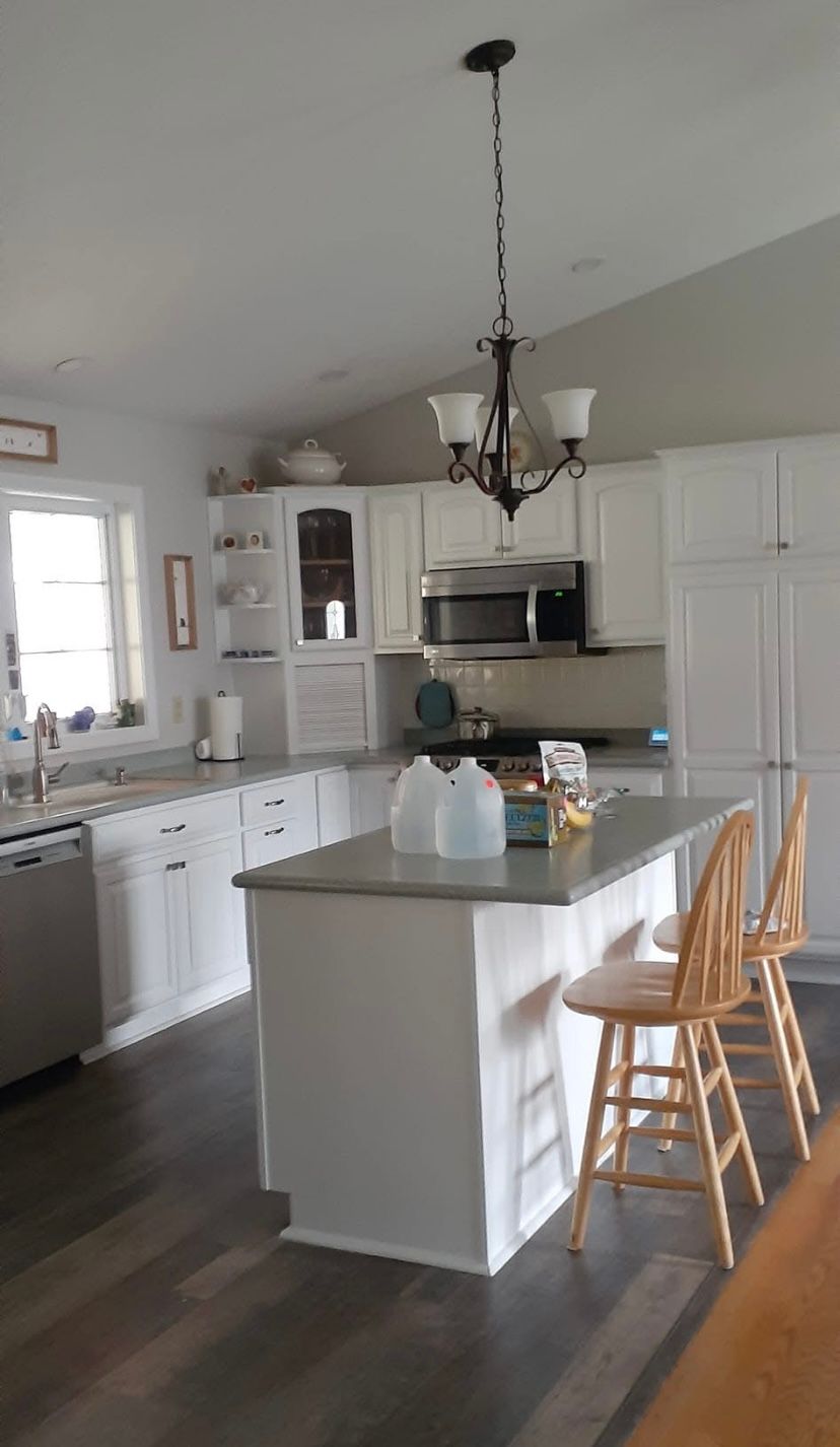 Bright white kitchen with island, pendant light, and wooden bar stools, viewed from the dining area