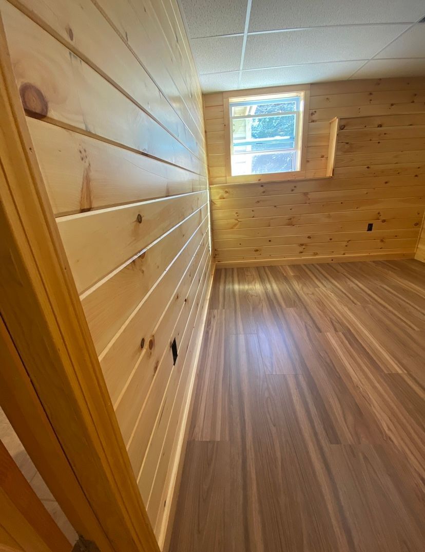 Wood-paneled empty room with sloped ceiling, wood floor, and a small window.
