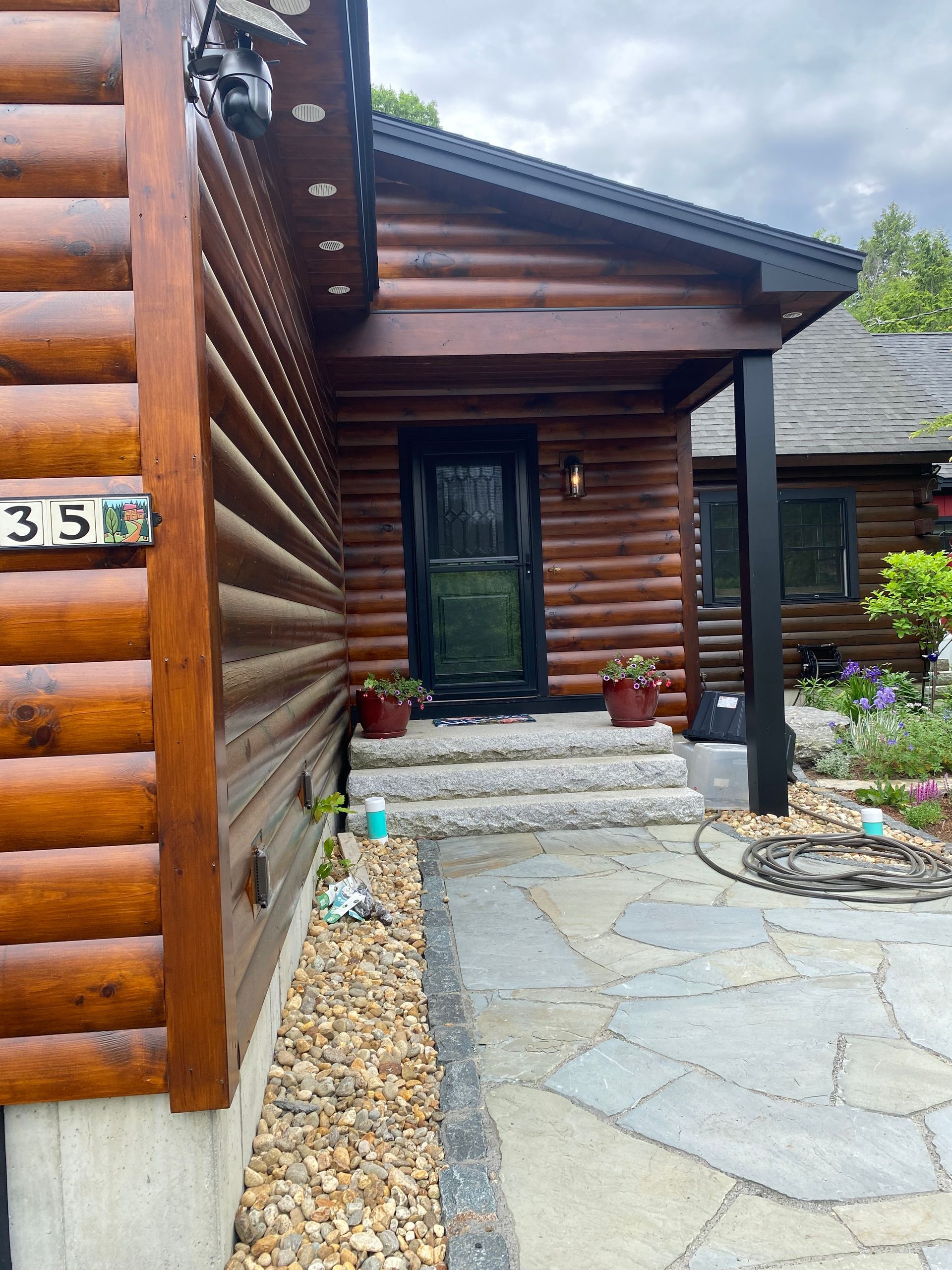 Front entry of a log cabin with stone walkway, dark door, and potted plants under a covered porch