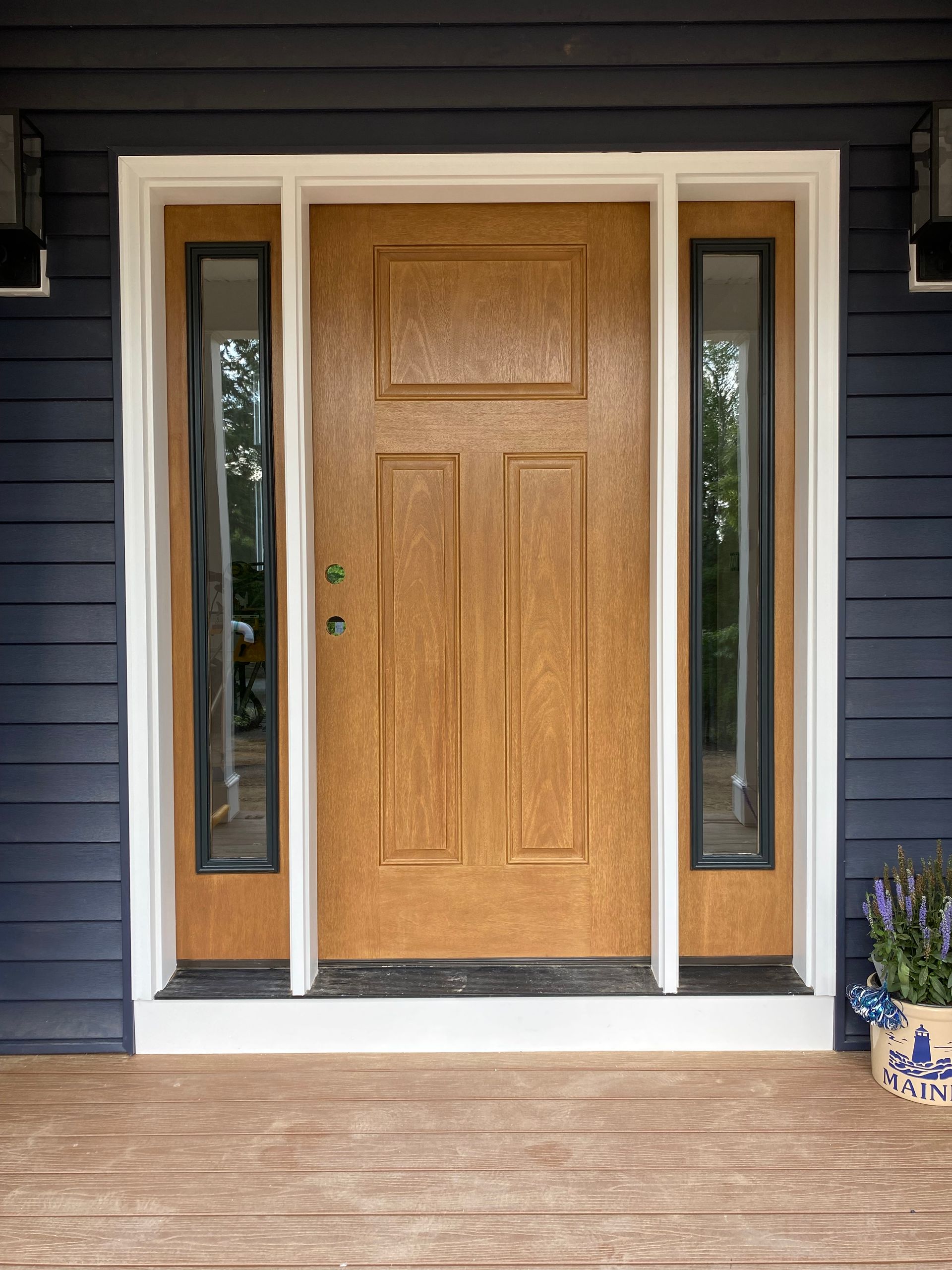Wooden front door with sidelights on a dark blue house exterior, viewed from the porch