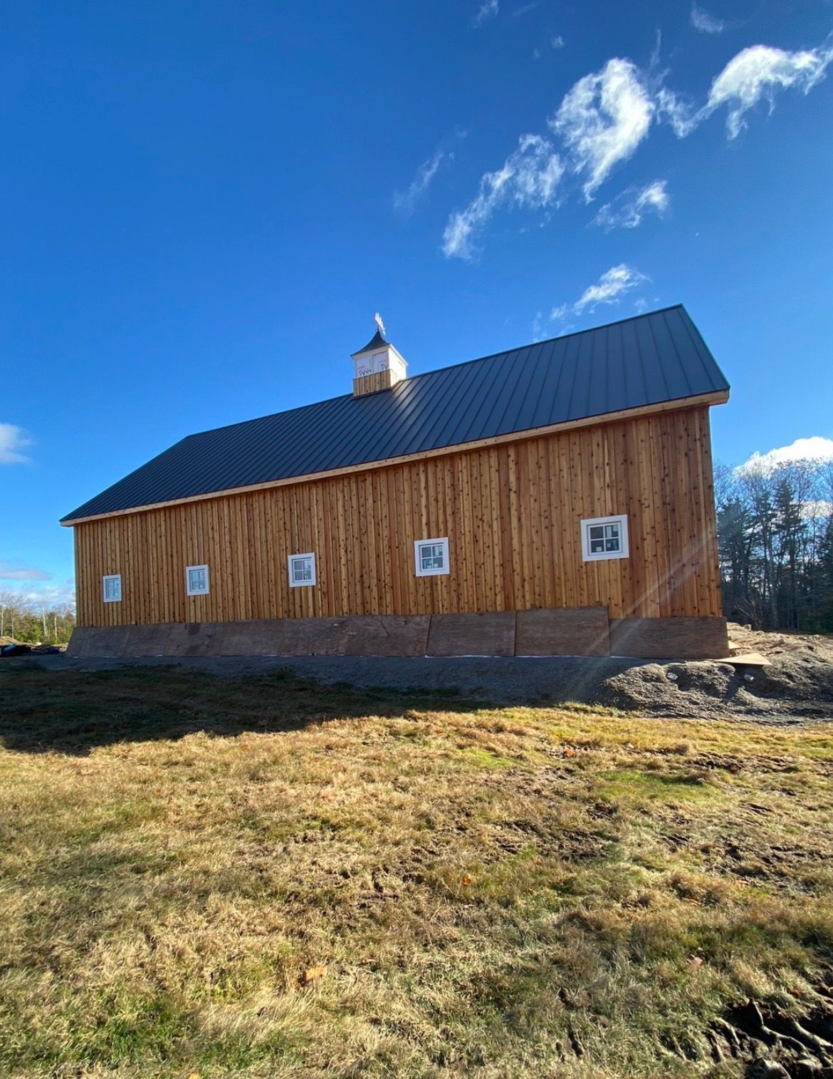 Wooden barn with a blue metal roof on a grassy hill under a bright blue sky.