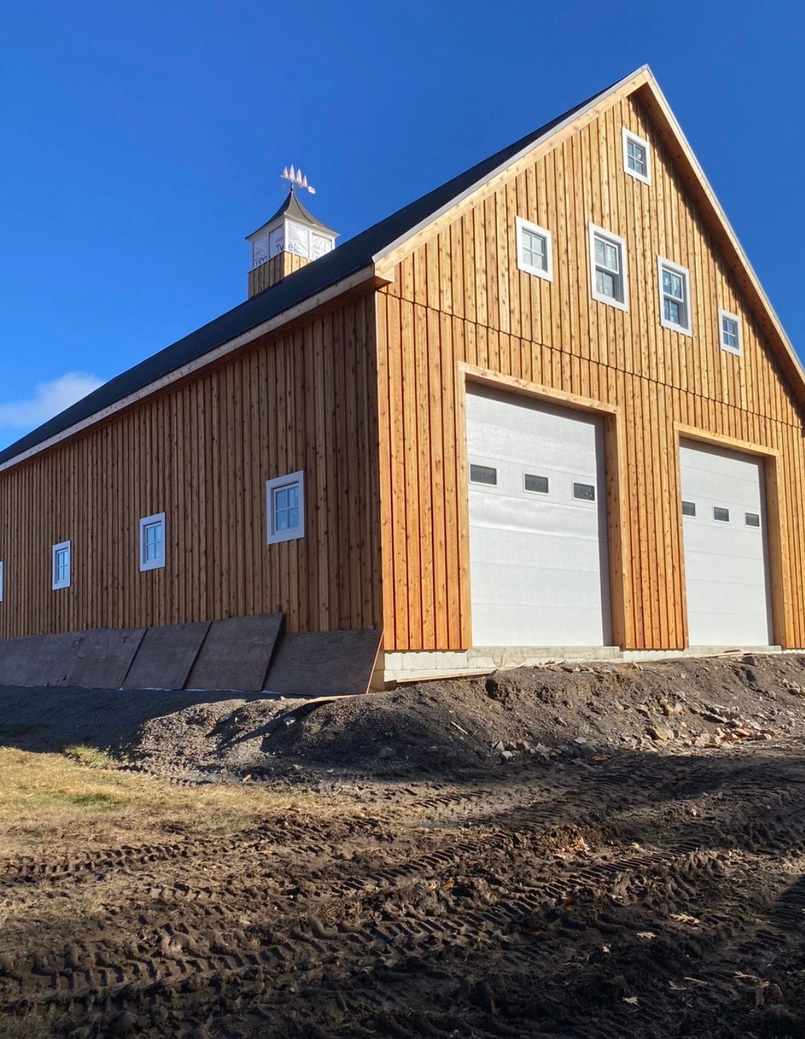 Wooden barn with two white garage doors and a steep roof under a clear blue sky.