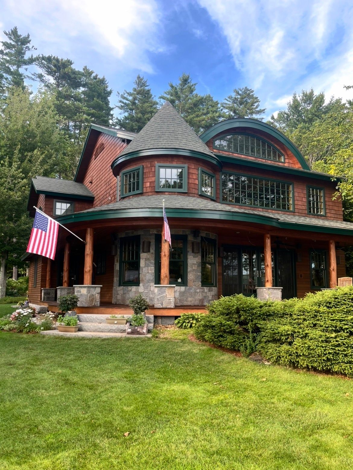 Victorian-style house with red trim and American flags, set on a lush green lawn under trees