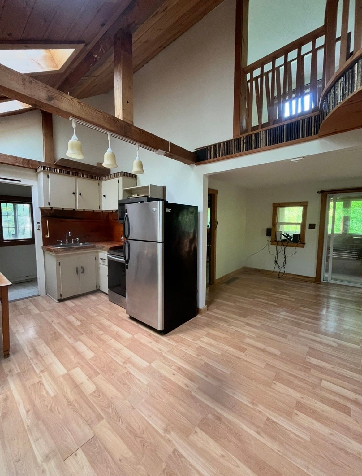 Open loft-style kitchen and living area with wood floors, stainless fridge, and exposed beams