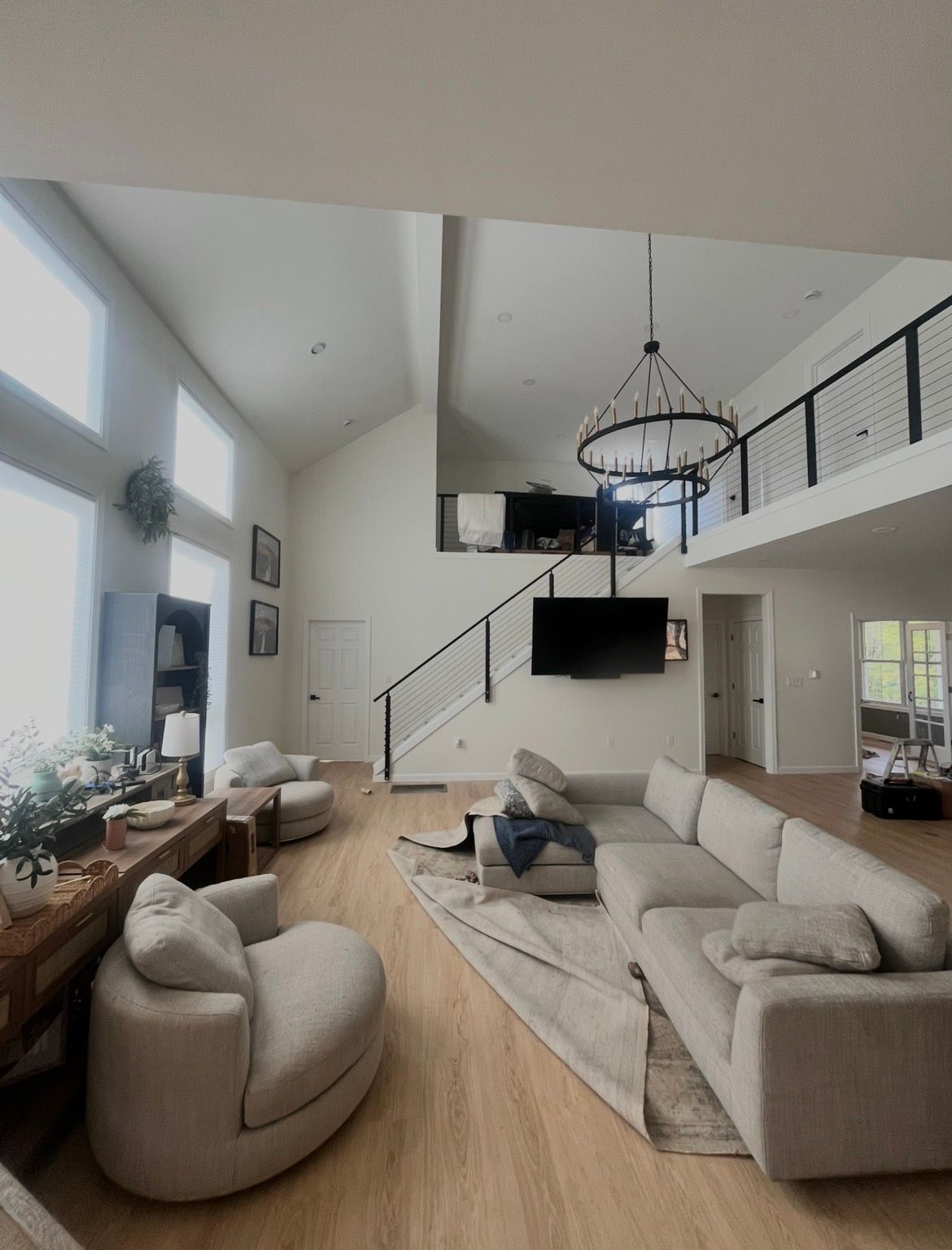 Modern living room with vaulted ceiling, beige sofa, chaise chair, fireplace, and staircase overlooking the space