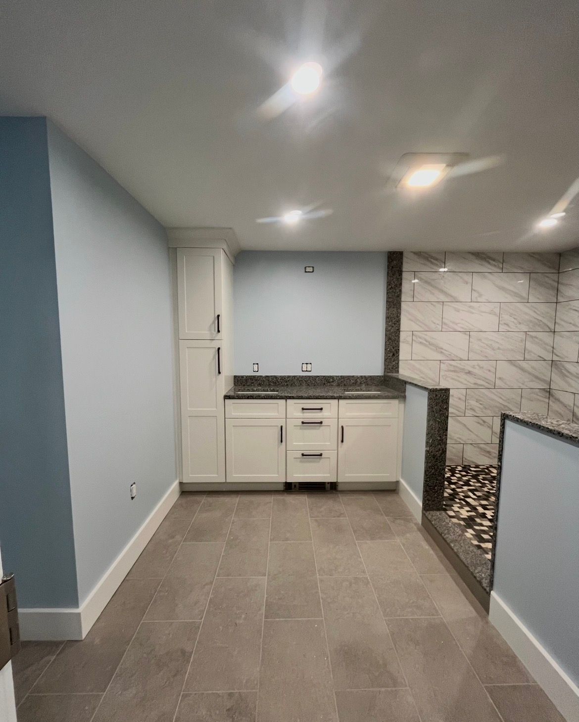 Small modern kitchen with white cabinets, gray tile floor, and light blue walls.
