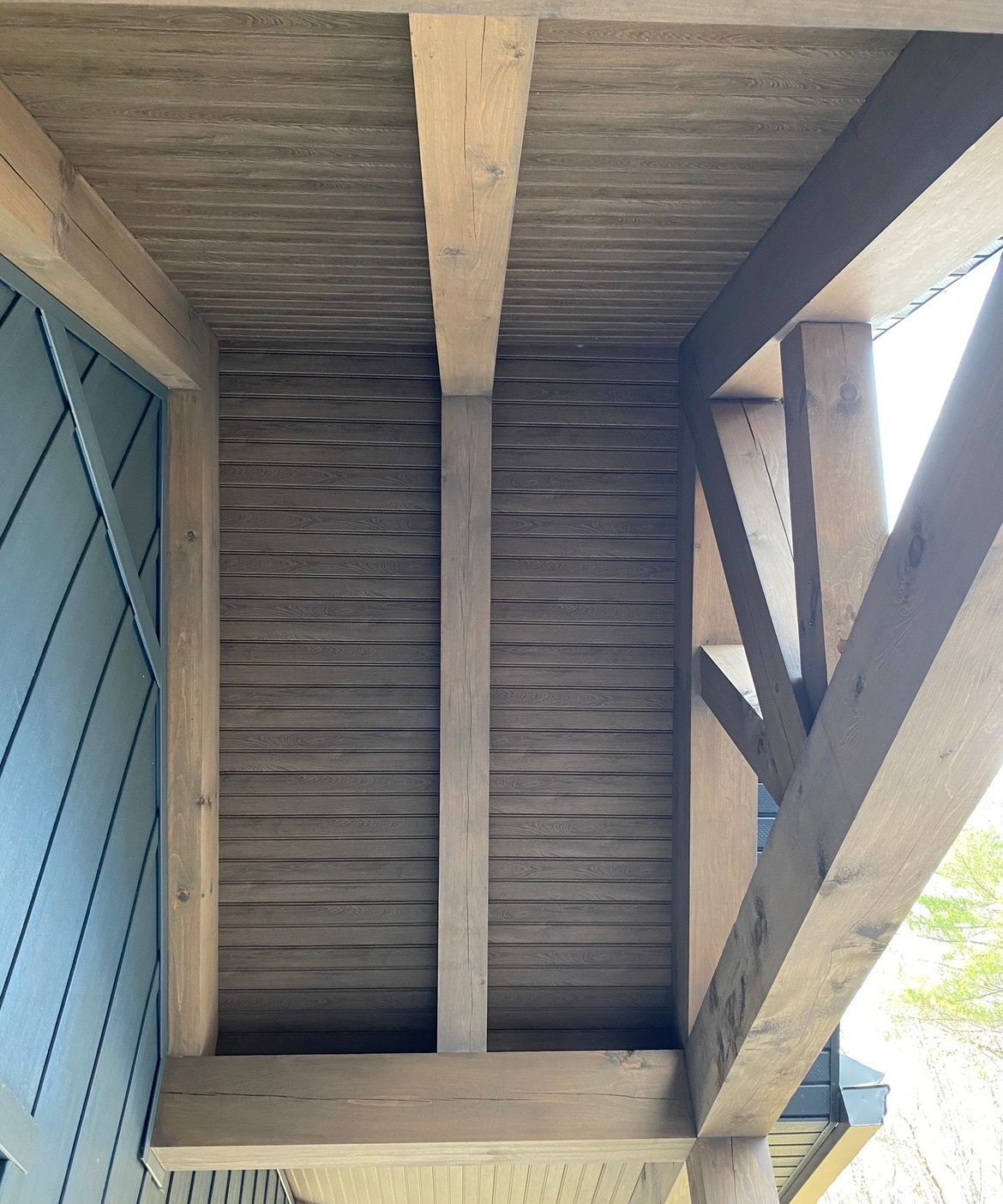 Underside of a wooden roof with beams, weathered planks, and a blue door on the left.