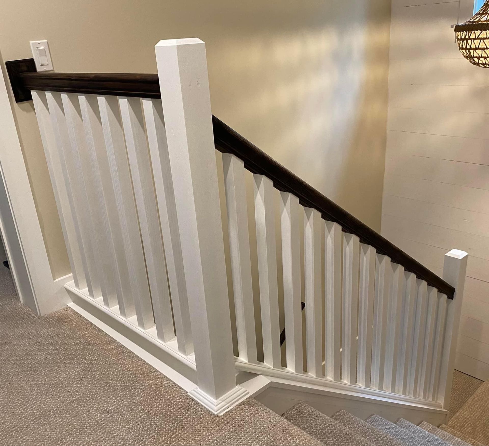 White staircase railing with black handrail on a carpeted indoor stairway.