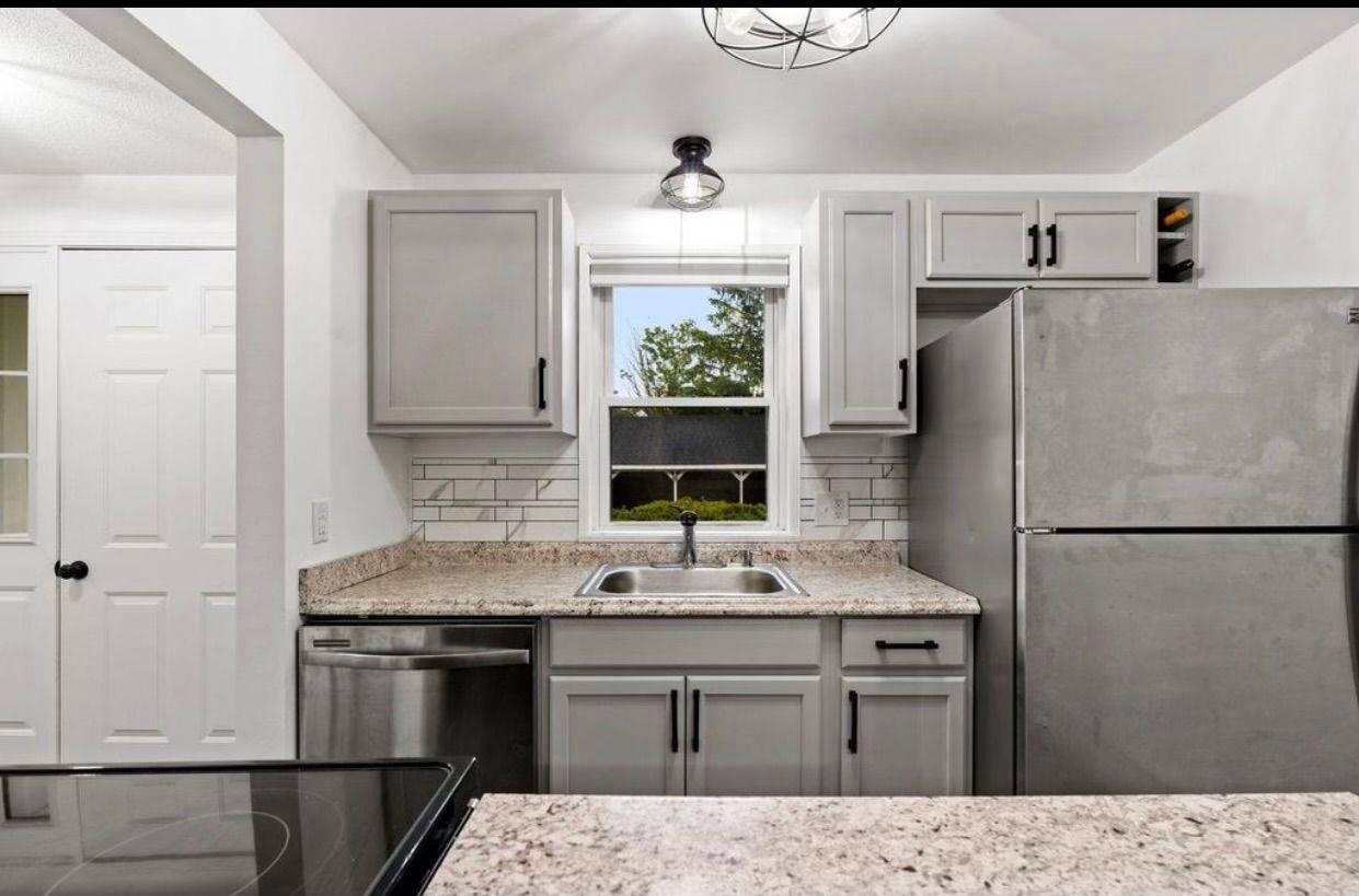 Modern kitchen with gray cabinets, granite counters, window over sink, and stainless steel appliances