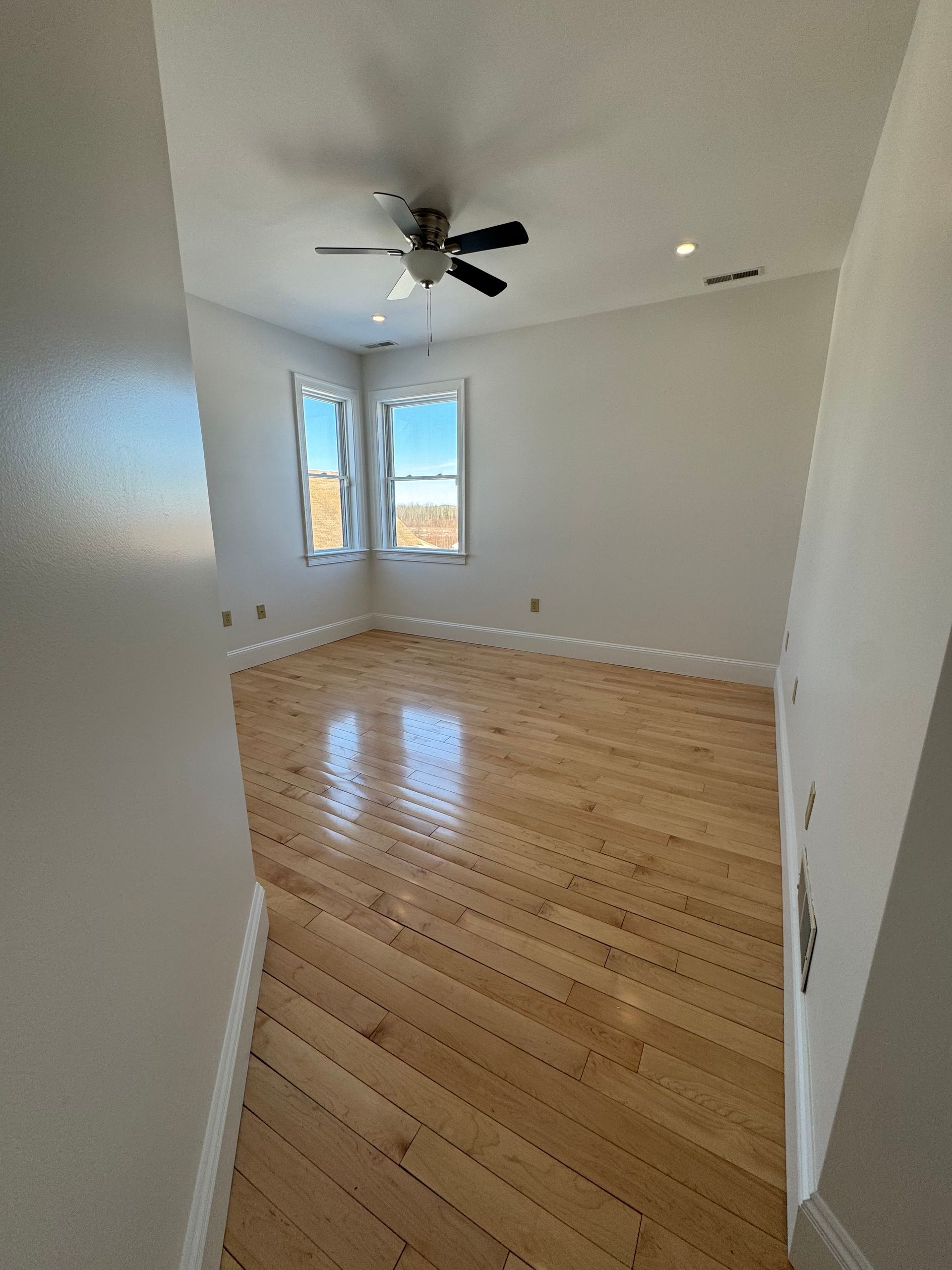 An empty bedroom with hardwood floors and a ceiling fan.