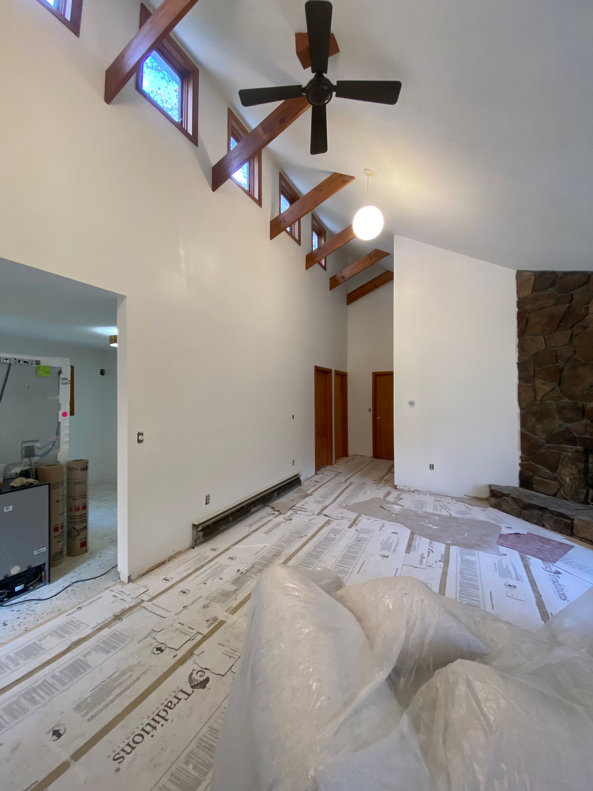 Living room under renovation with ladder, ceiling fan, exposed beams, and plastic-covered furniture