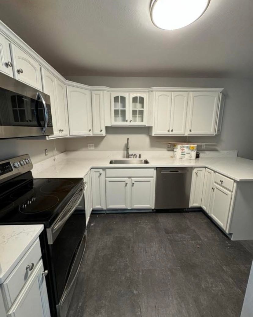 White kitchen with black appliances, gray floor, and L-shaped countertops with sink and dishwasher.