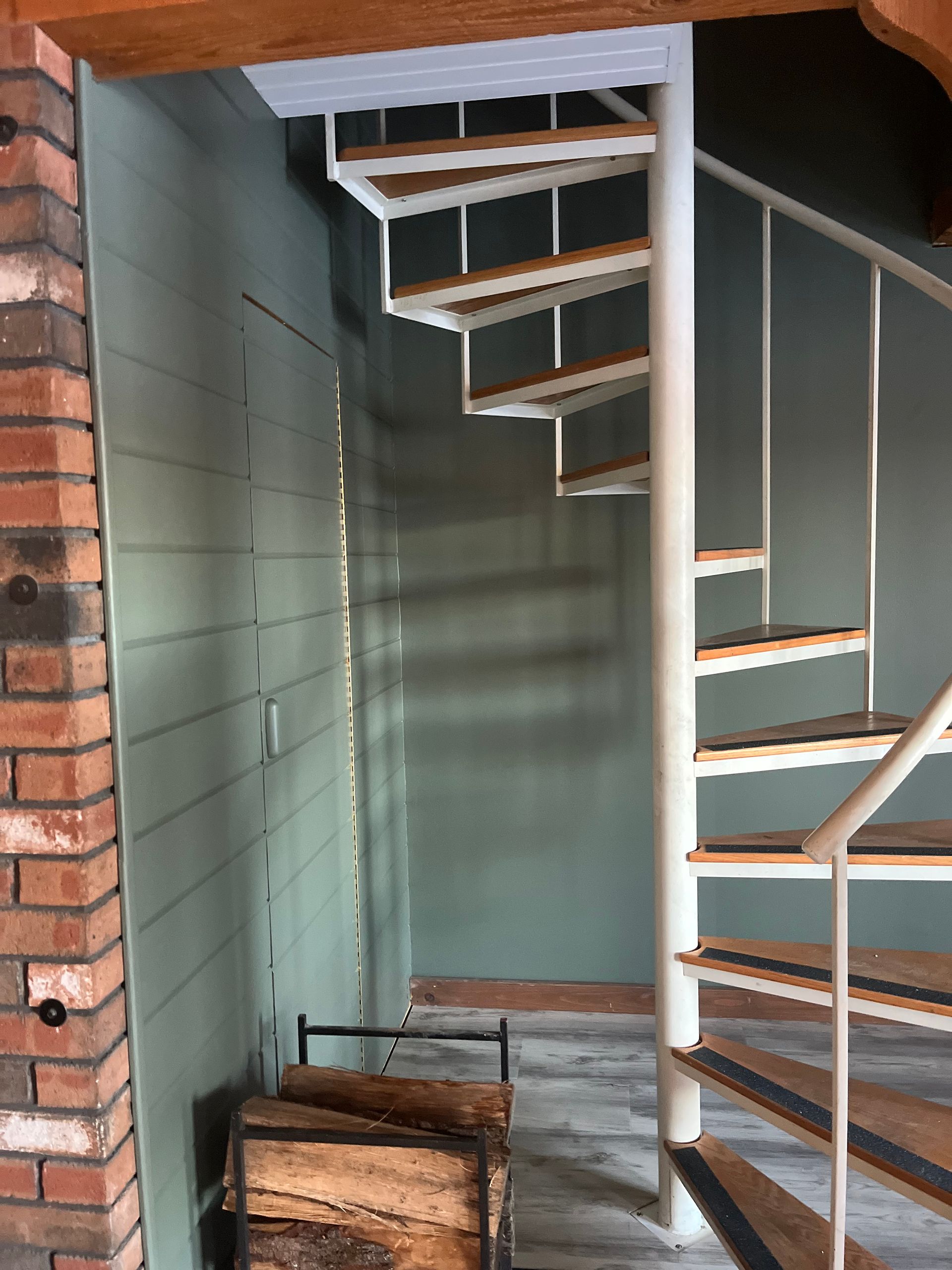 Partially built wooden staircase in an unfinished interior room with green walls and exposed brick edge