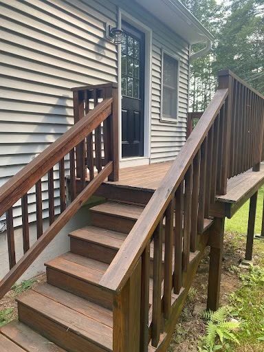 Wooden front steps and porch ramp leading to a house entrance with brown railing and beige siding