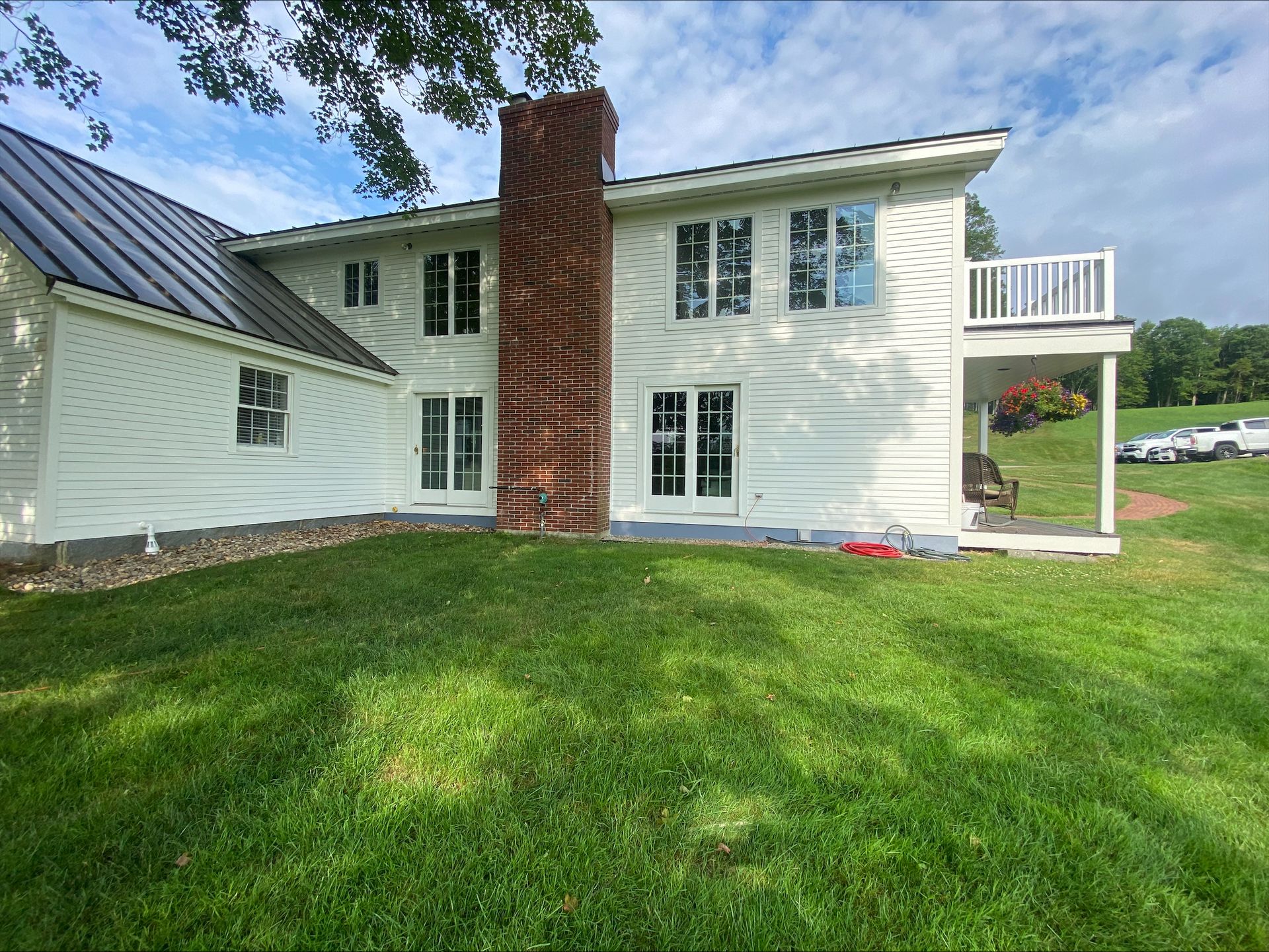 White two-story house with brick chimney, white balcony, and green lawn under a blue sky.