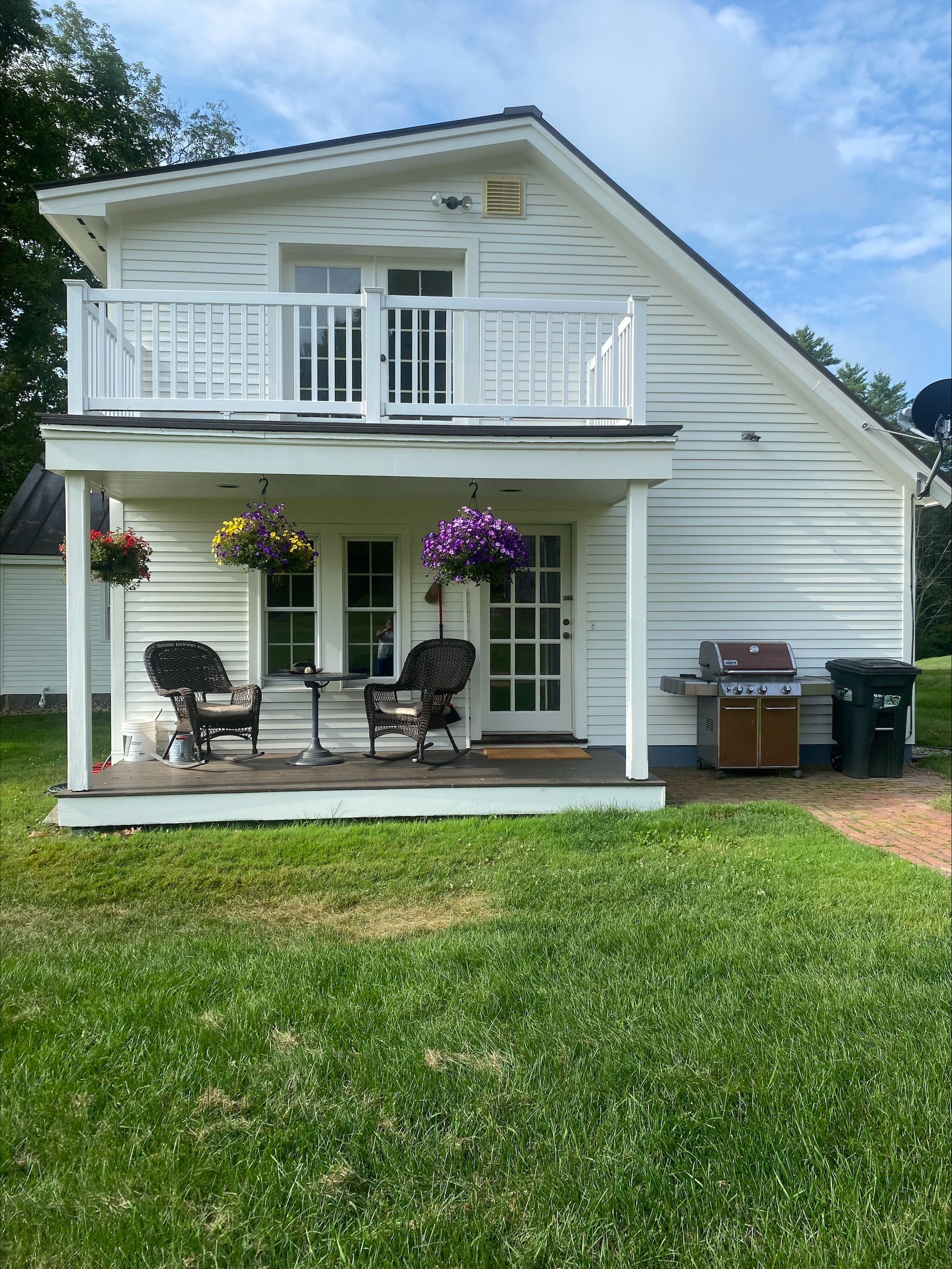 White two-story house with a porch and balcony, hanging flower baskets, and a green lawn in front