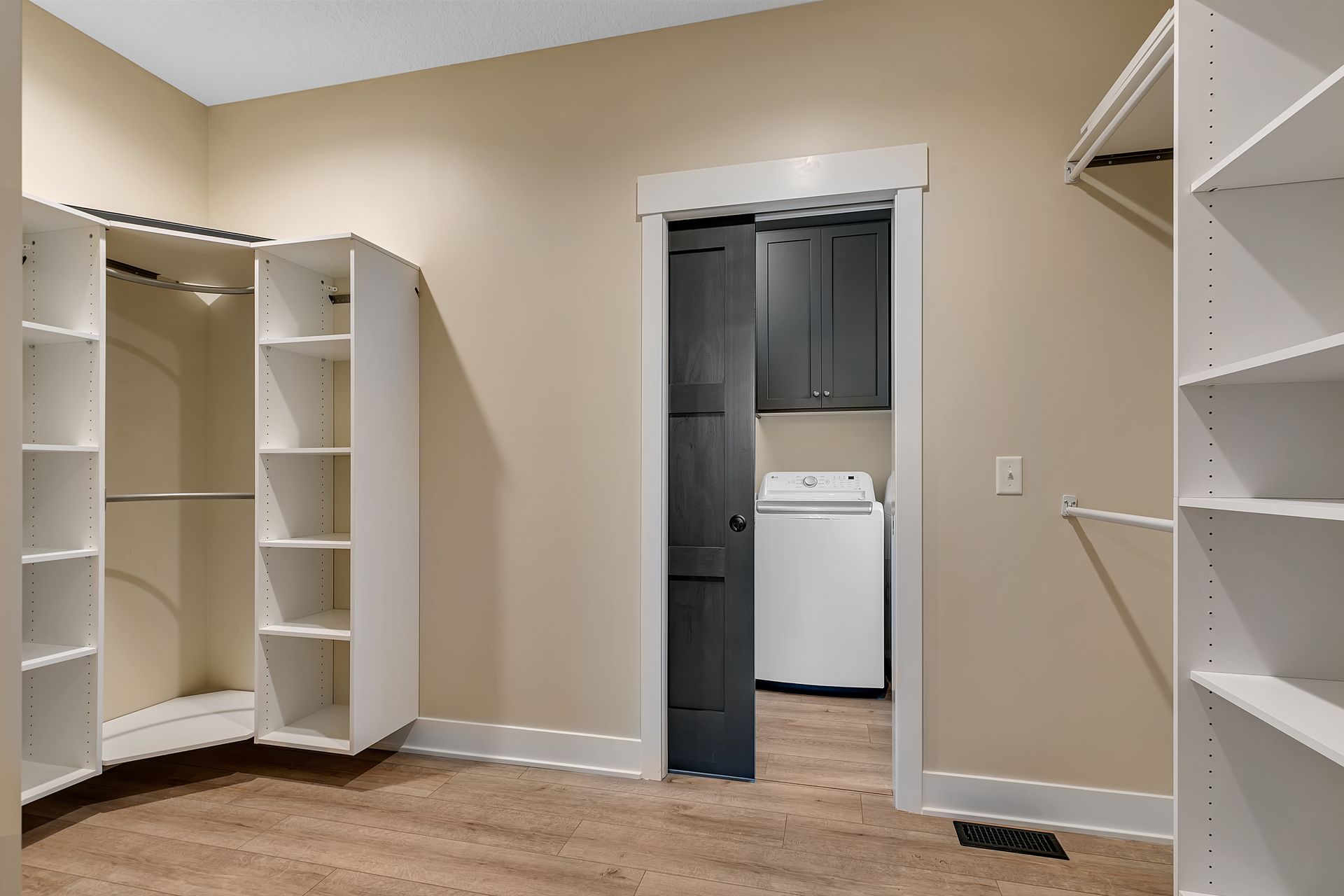 A walk in closet with a laundry room in the background.