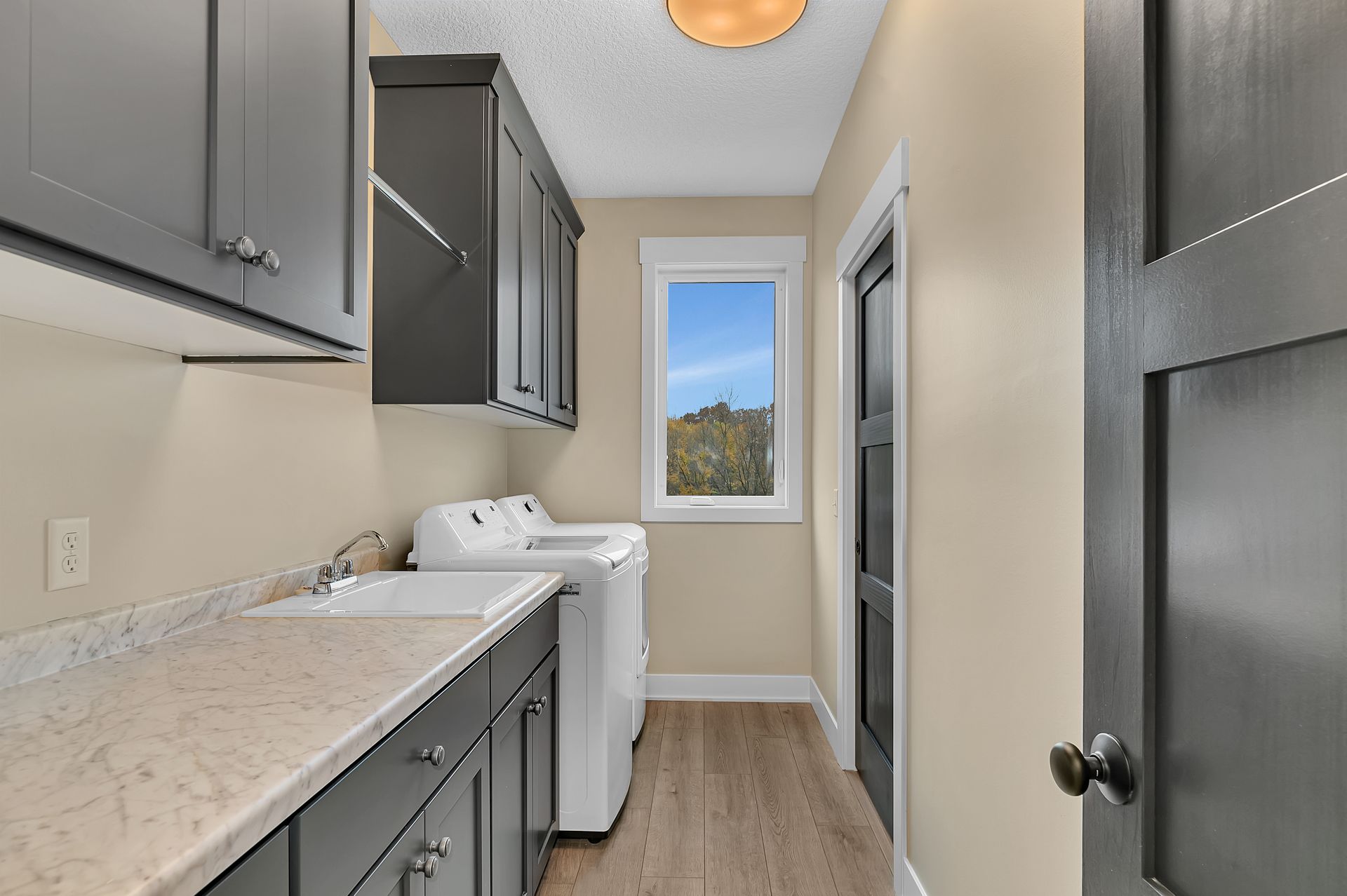 A laundry room with a washer and dryer , sink , cabinets and a window.