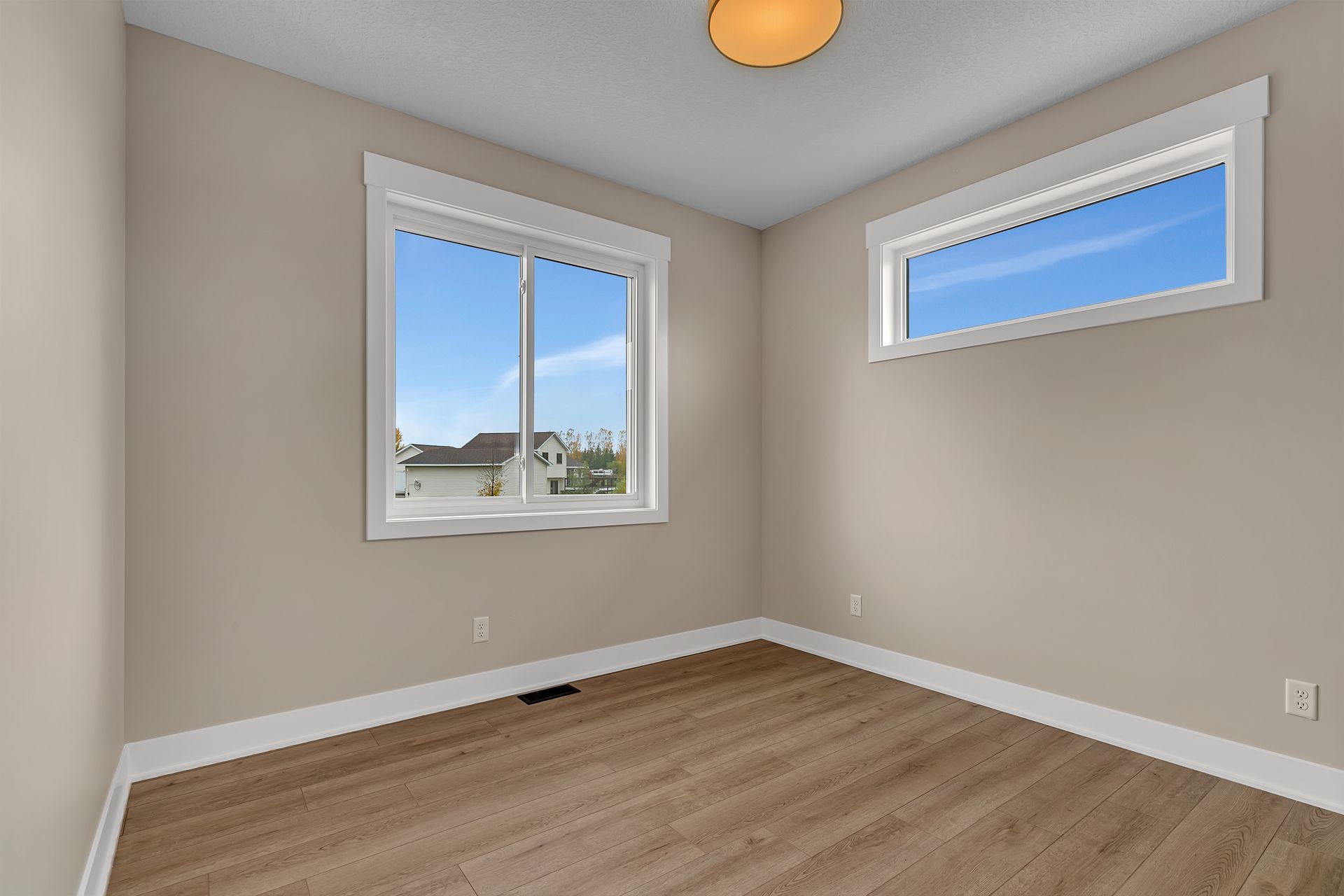An empty room with two windows and a wooden floor.