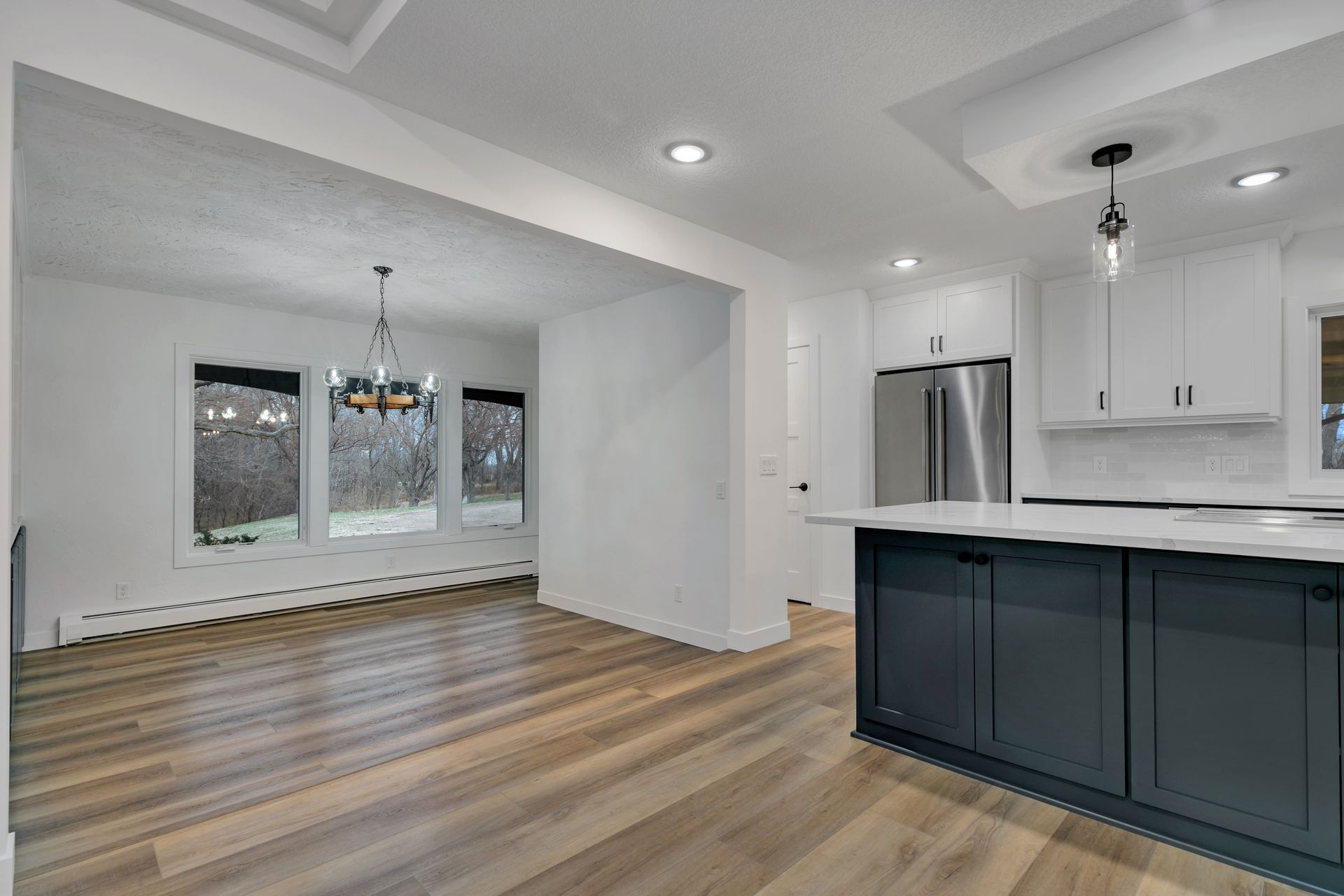 A kitchen with hardwood floors , white cabinets , stainless steel appliances and a large island.