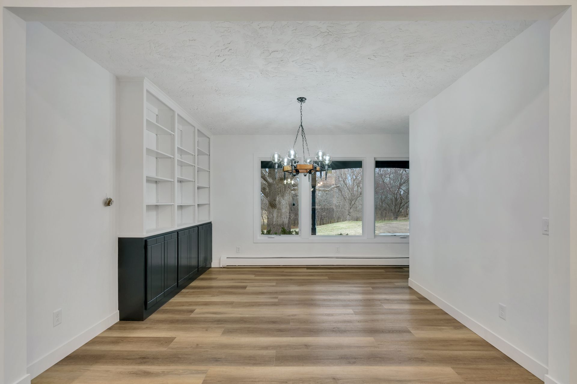 An empty living room with hardwood floors and a chandelier.