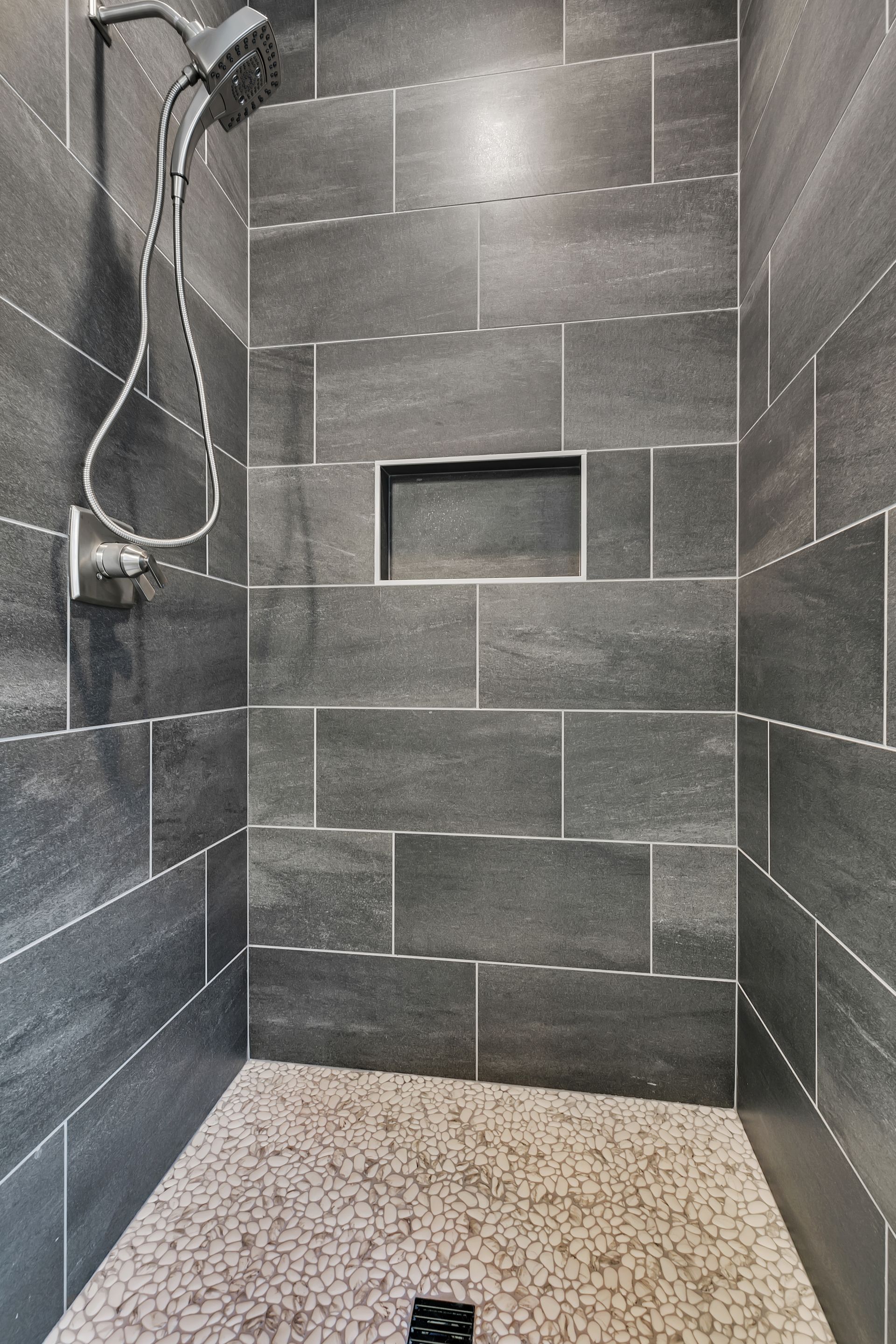 A shower with a shower head and a drain on the floor.