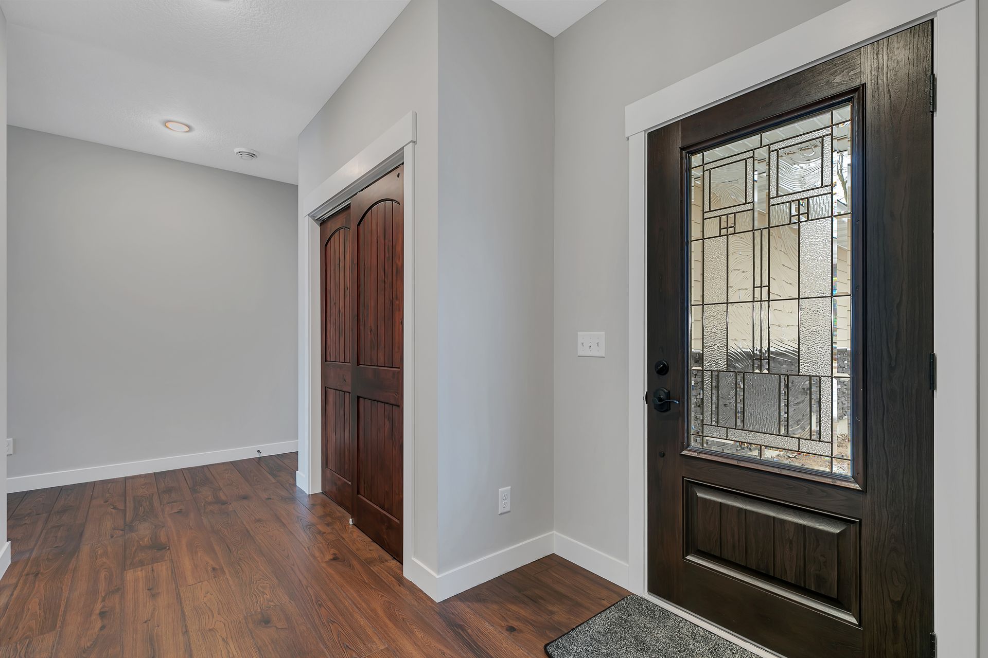 A hallway with hardwood floors and a door with a stained glass window.