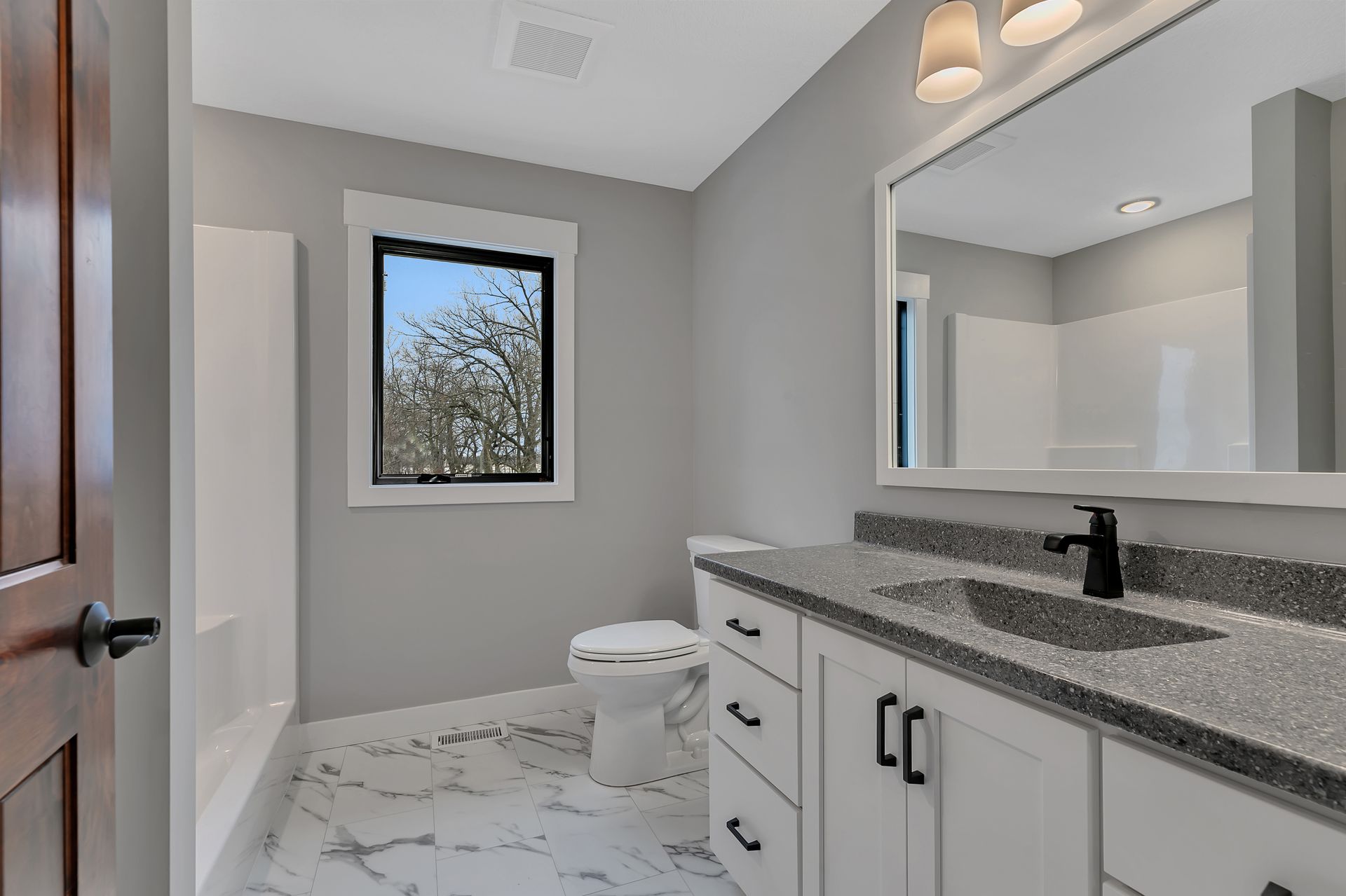 A bathroom with a toilet , sink , mirror and window.