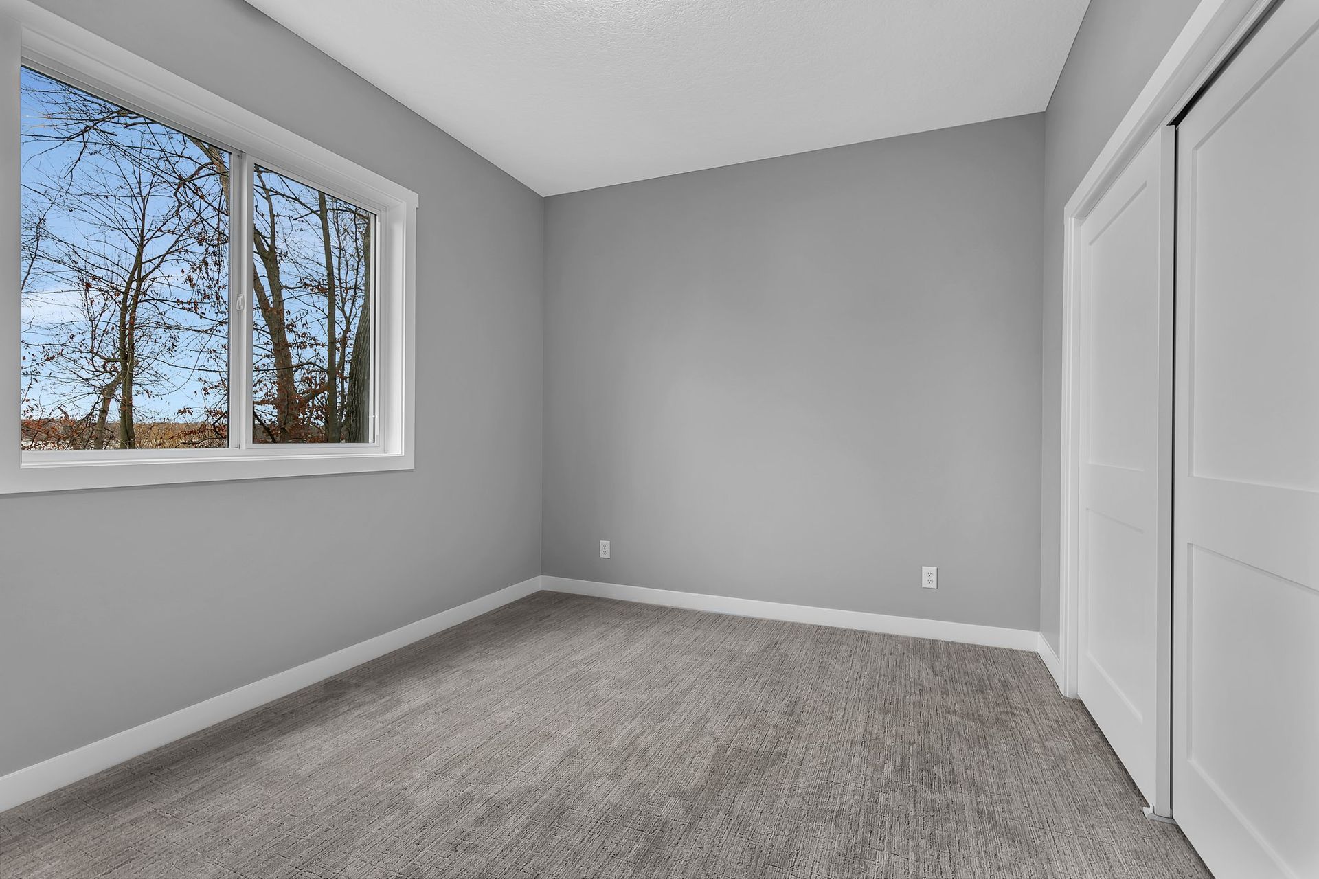 An empty bedroom with gray walls and a window.